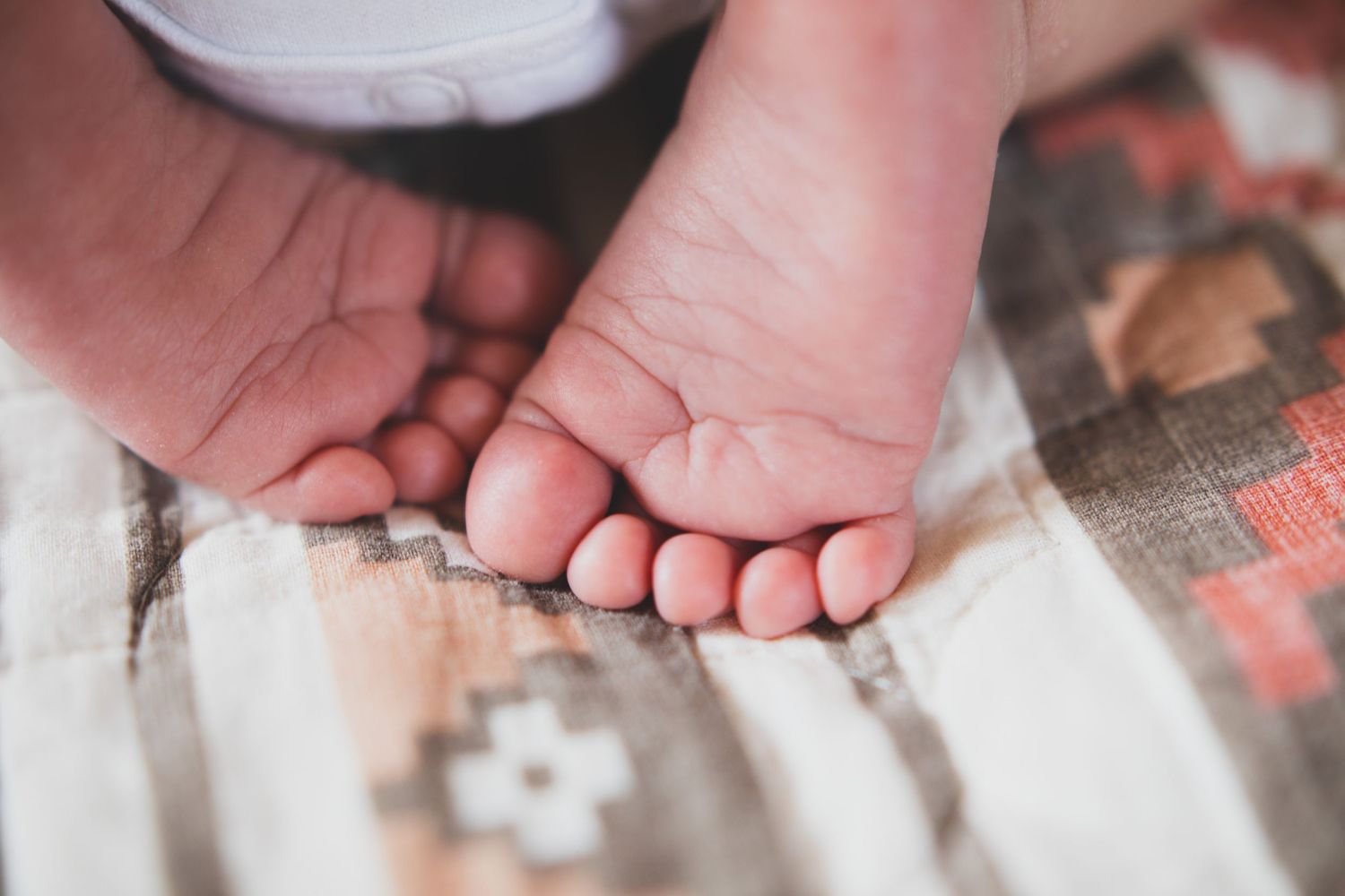 Close-up of a newborn baby's tiny feet resting in a parent's gentle hands on a patterned blanket.