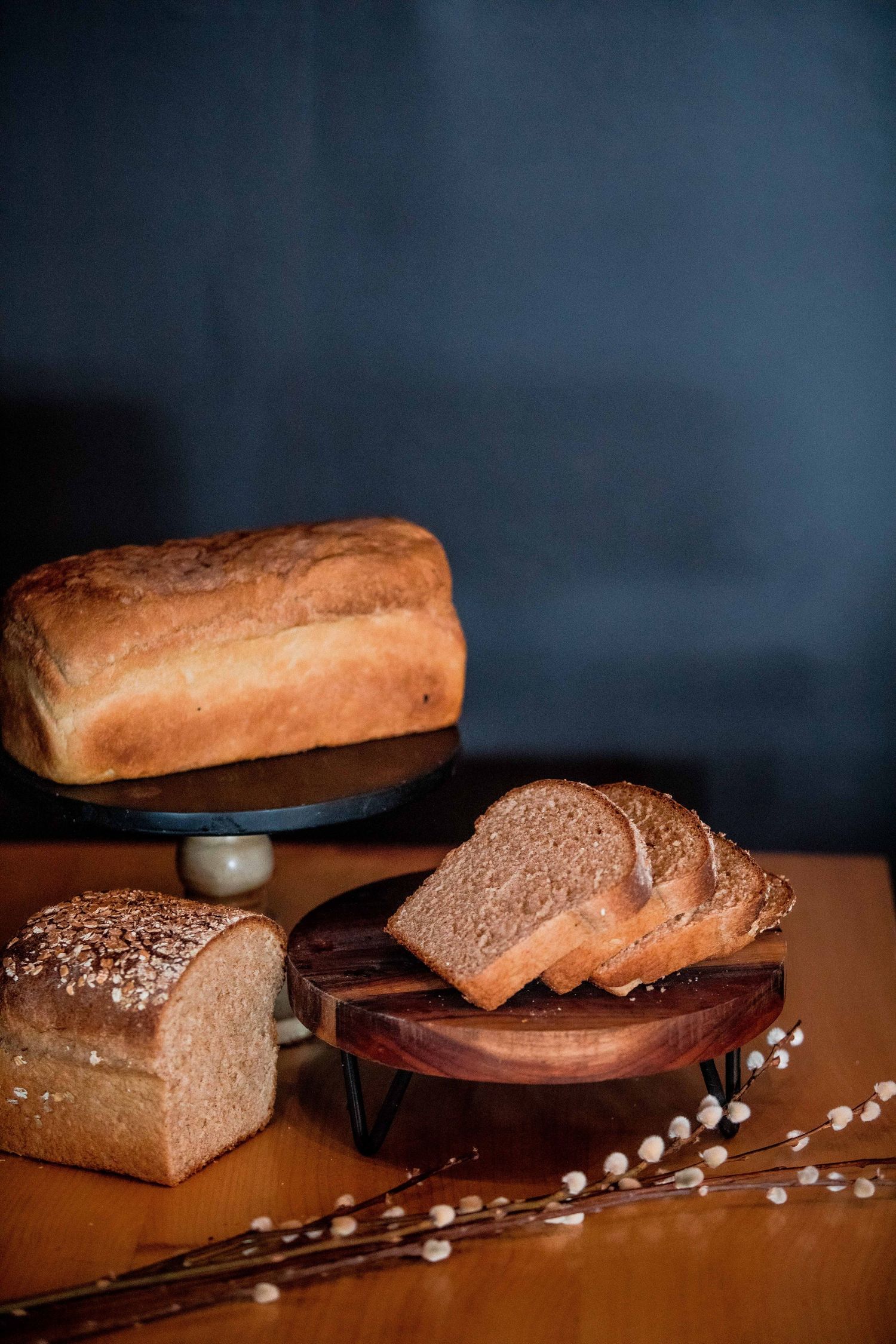 Rustic artisan bread loaves and slices on wooden boards with pussy willow branches on a dark background.