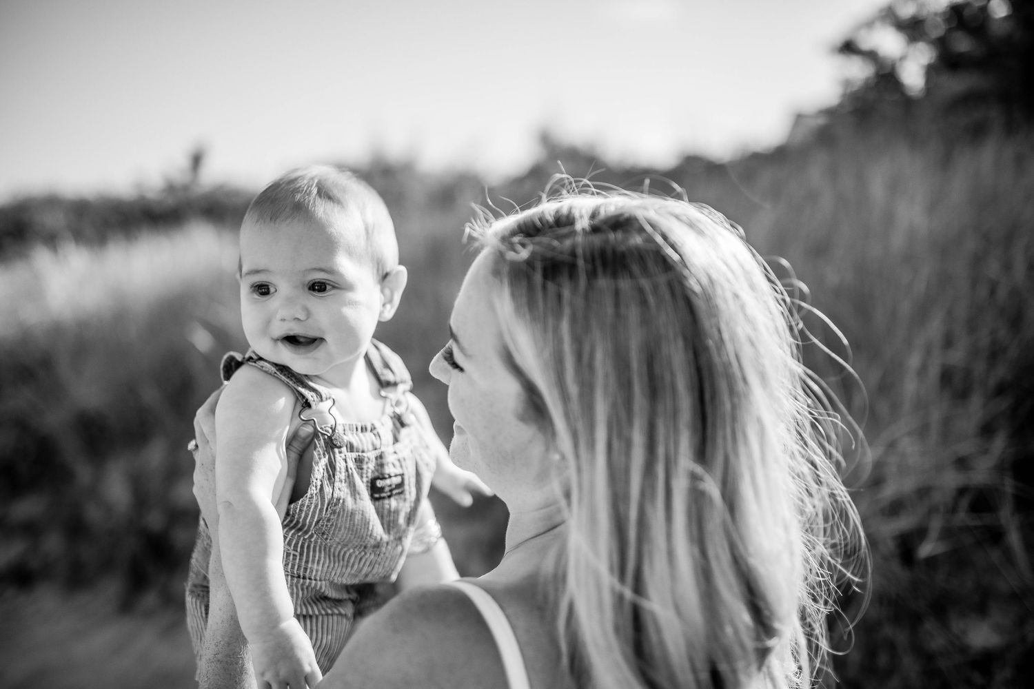 Black and white photo of mother holding laughing baby by Cape Cod sand dunes.