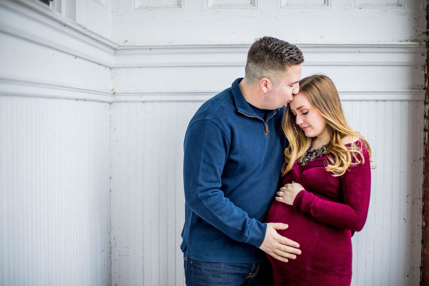 Couple tenderly embracing while man kisses pregnant woman's forehead outdoors.