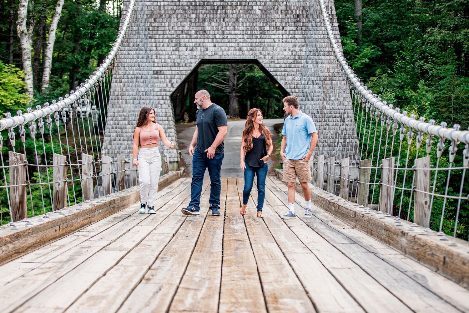 Family of four standing on historic suspension bridge surrounded by lush green trees.