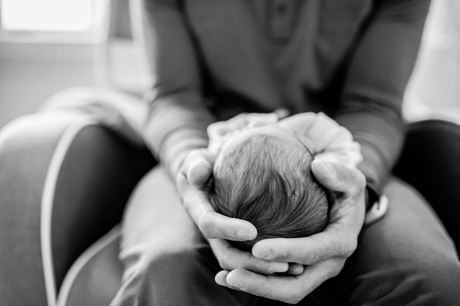 Black and white close-up of parent gently cradling newborn baby head in cupped hands.