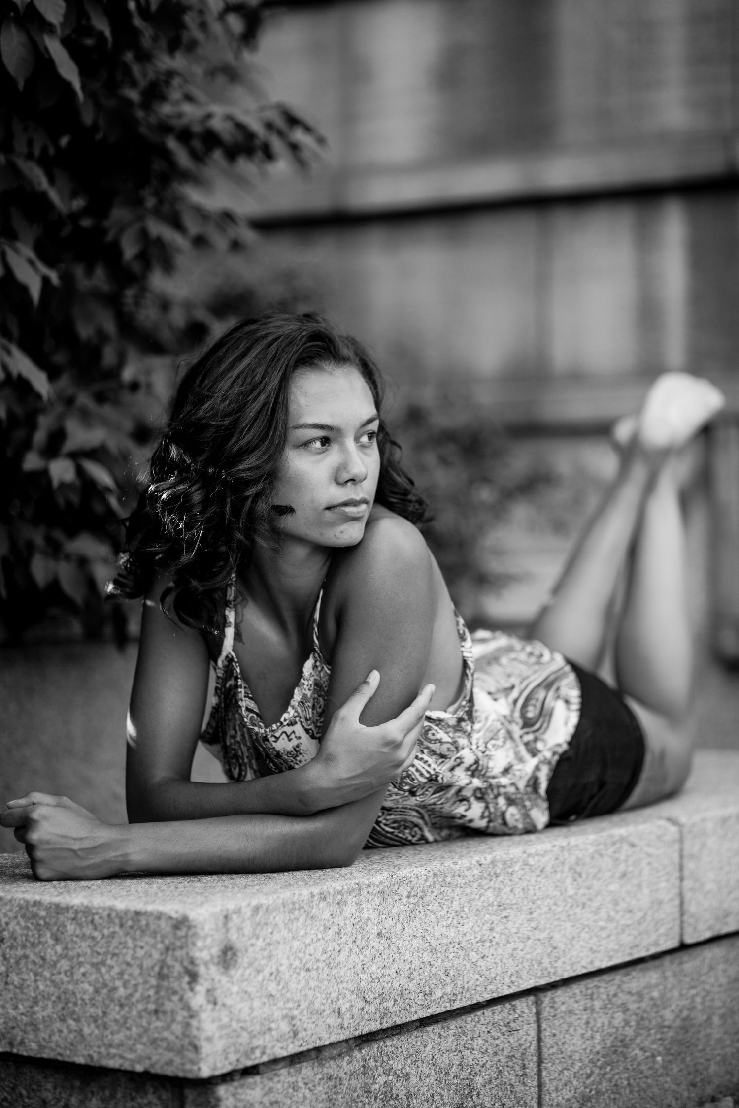 Black and white photo of a young woman lying on a stone ledge in a garden setting.
