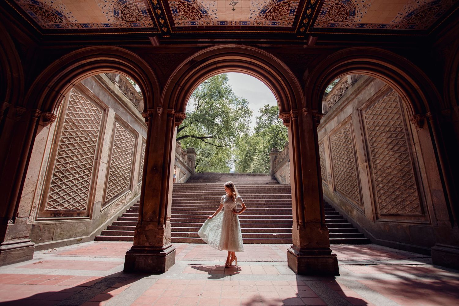 Woman in white dress standing under ornate arches of Bethesda Terrace in Central Park, New York.