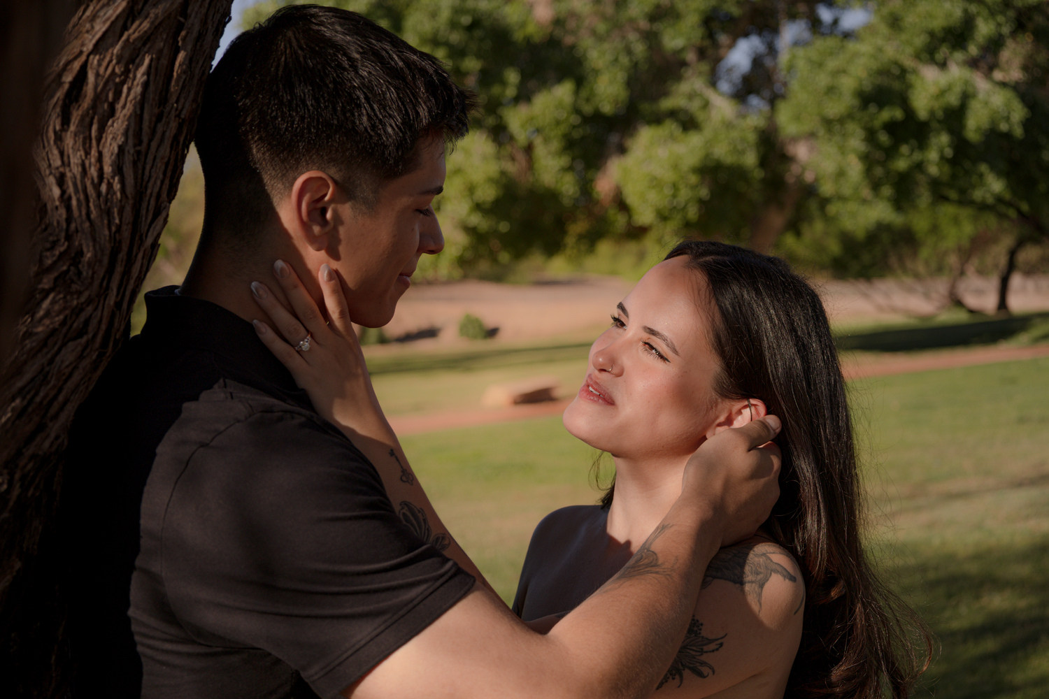 A professional photo, light colors, outdoors, a couple. A man tucking a womans hair behind her ear while lovingly gazing at her.