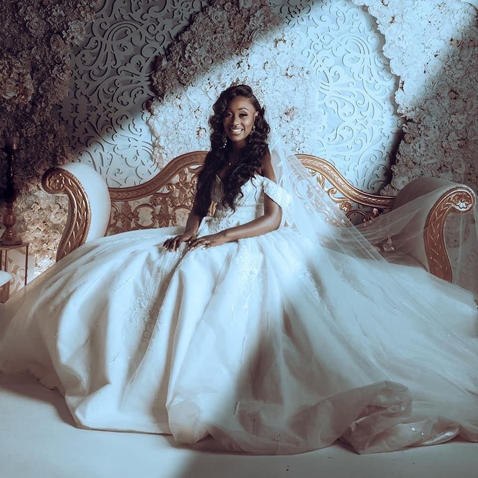 Ethereal bridal portrait with flowing white dress against textured wall.