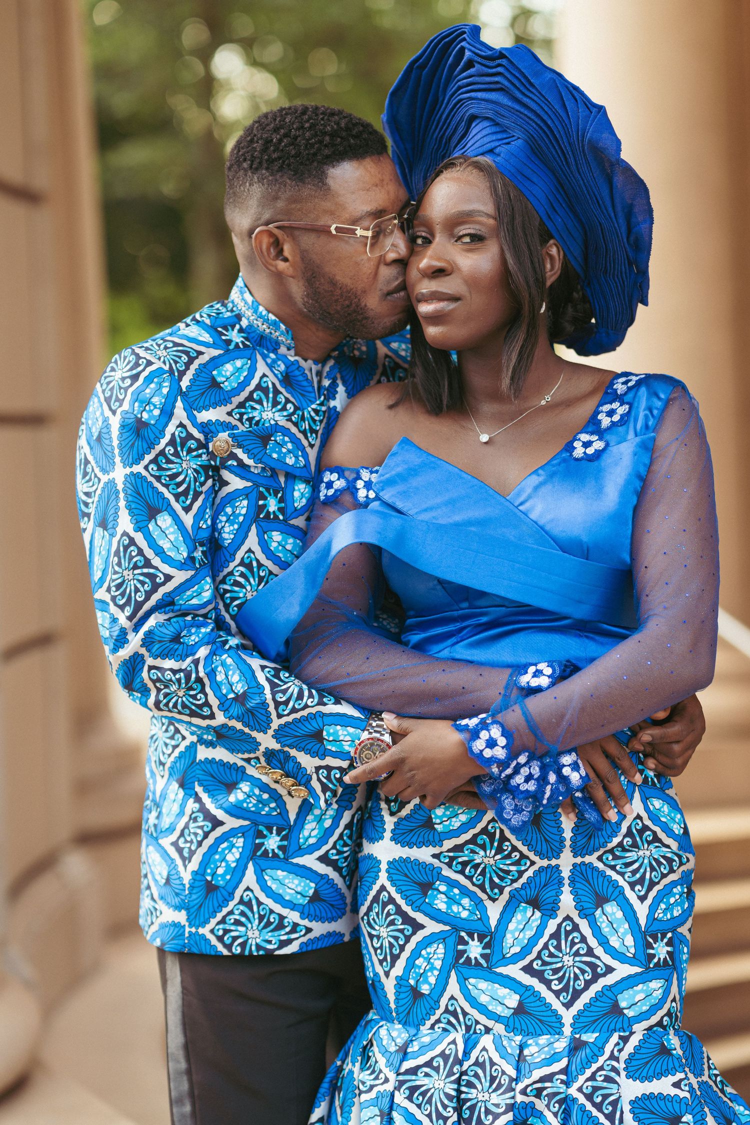 A couple wearing vibrant blue traditional African attire embrace during a romantic photoshoot.