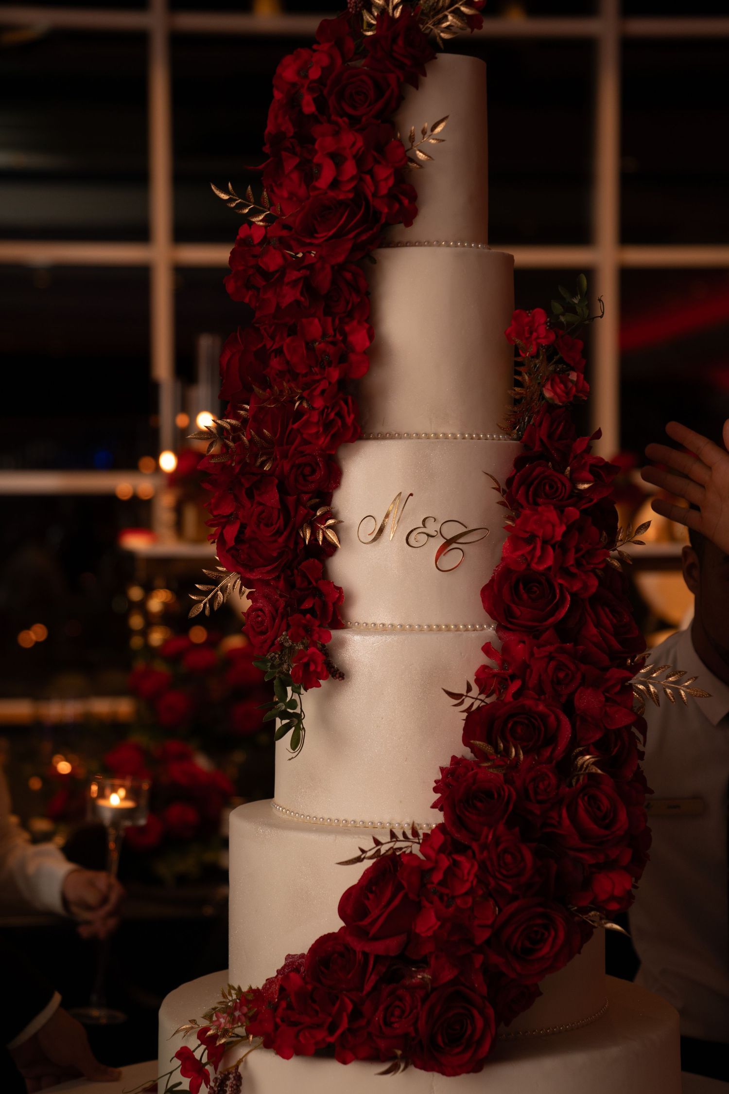 Elegant white wedding cake decorated with cascading deep red roses against a dark background.