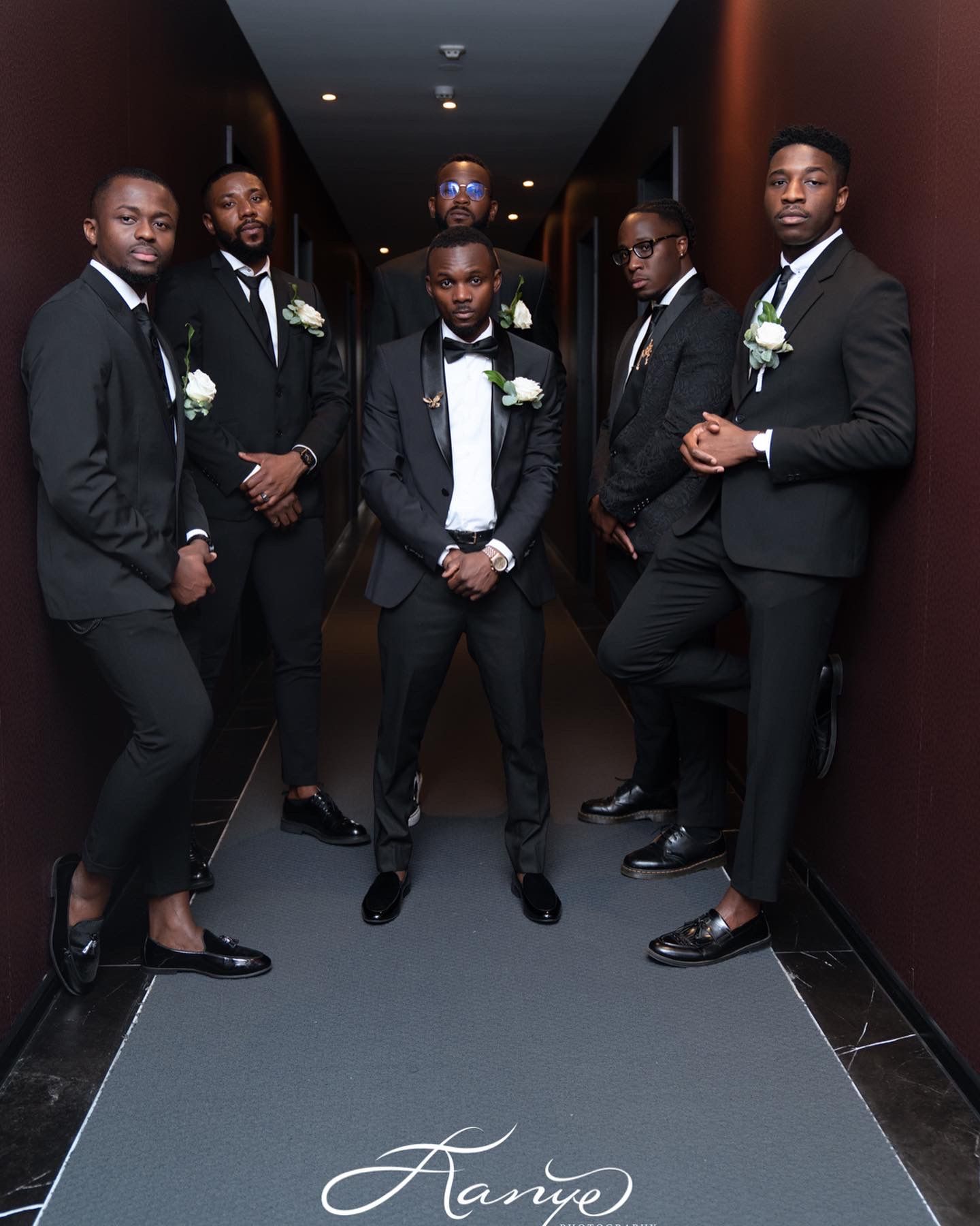 Groomsmen in black suits pose dramatically in dark hallway.
