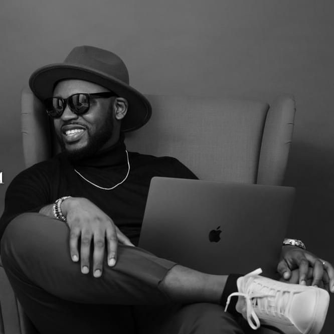 Casual portrait of person in hat working on laptop while relaxing in chair.