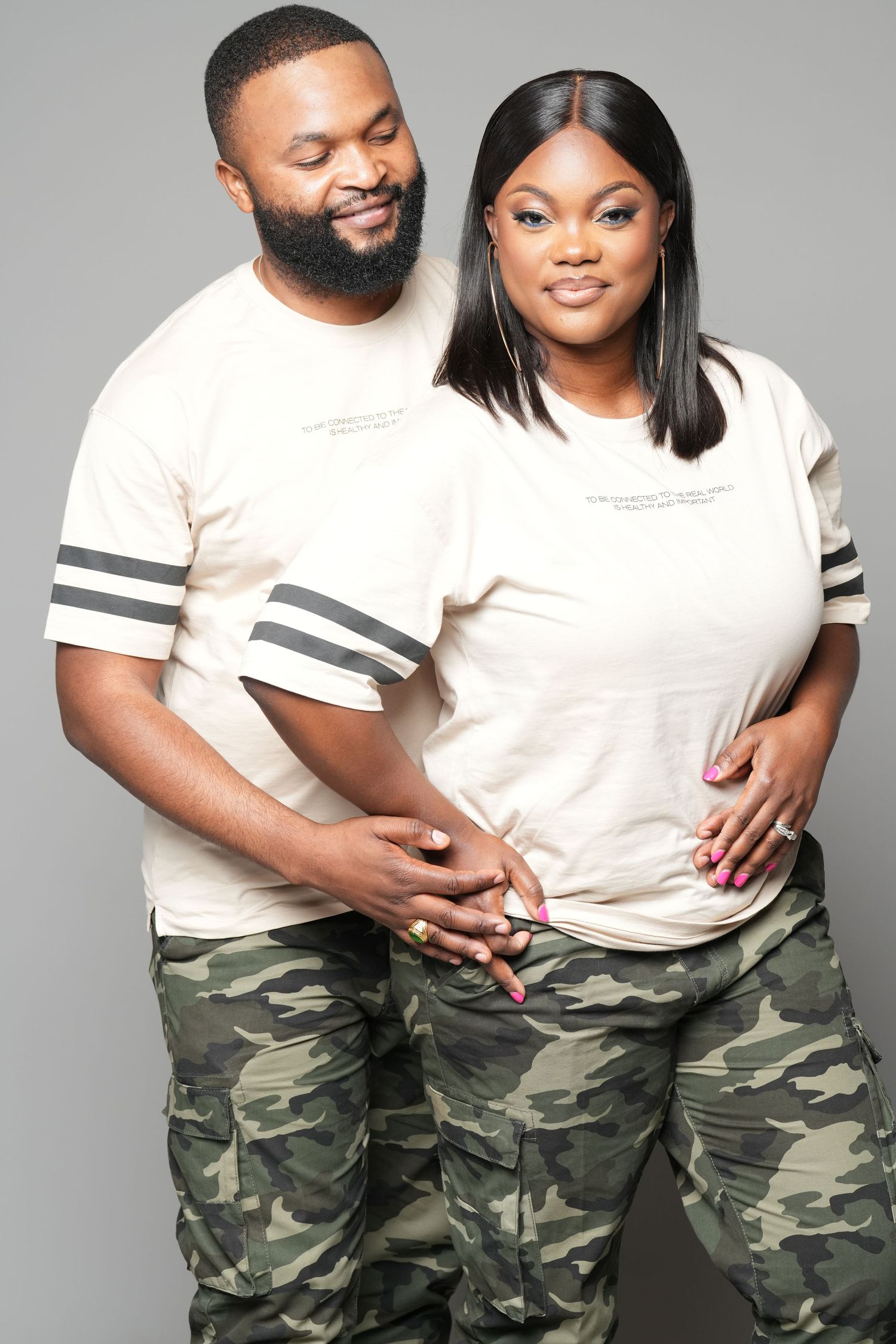 Couple wearing matching white t-shirts and camouflage pants pose playfully in studio portraits.