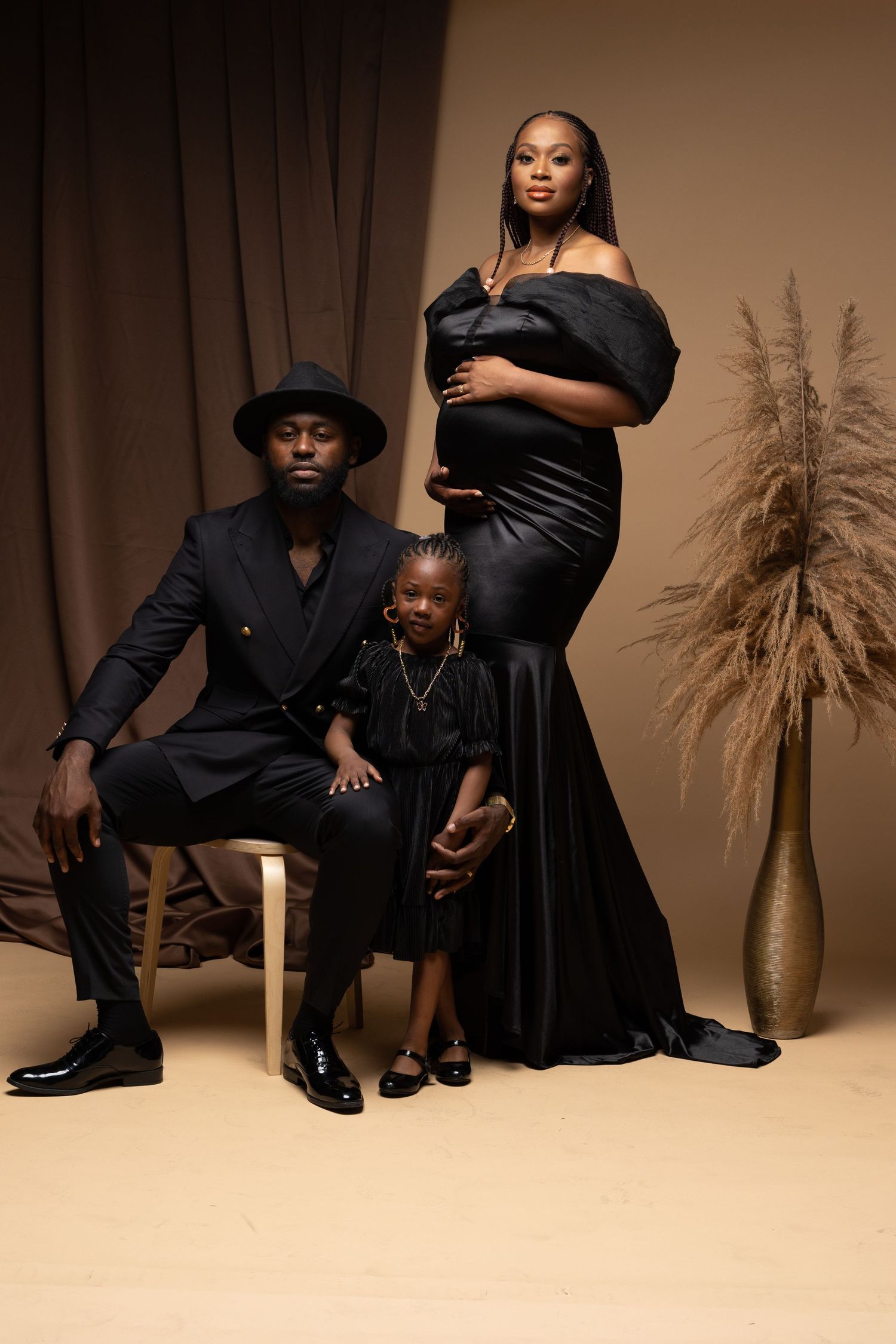 Studio portrait session with couple in elegant black attire posing against neutral backdrop with decorative pampas grass.