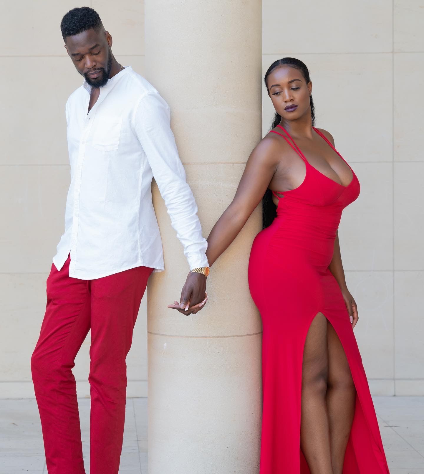 Stylish couple in contrasting red and white outfits pose against neutral wall.