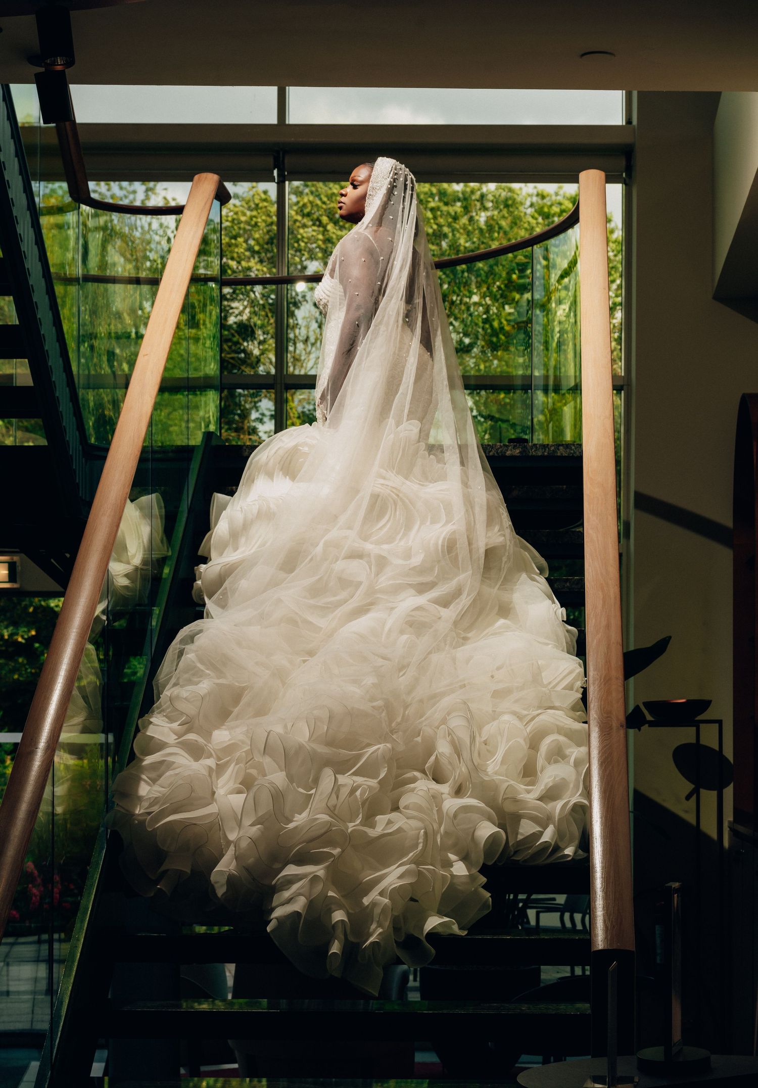 A dramatic silhouette of a wedding dress with ruffled layers against large windows.