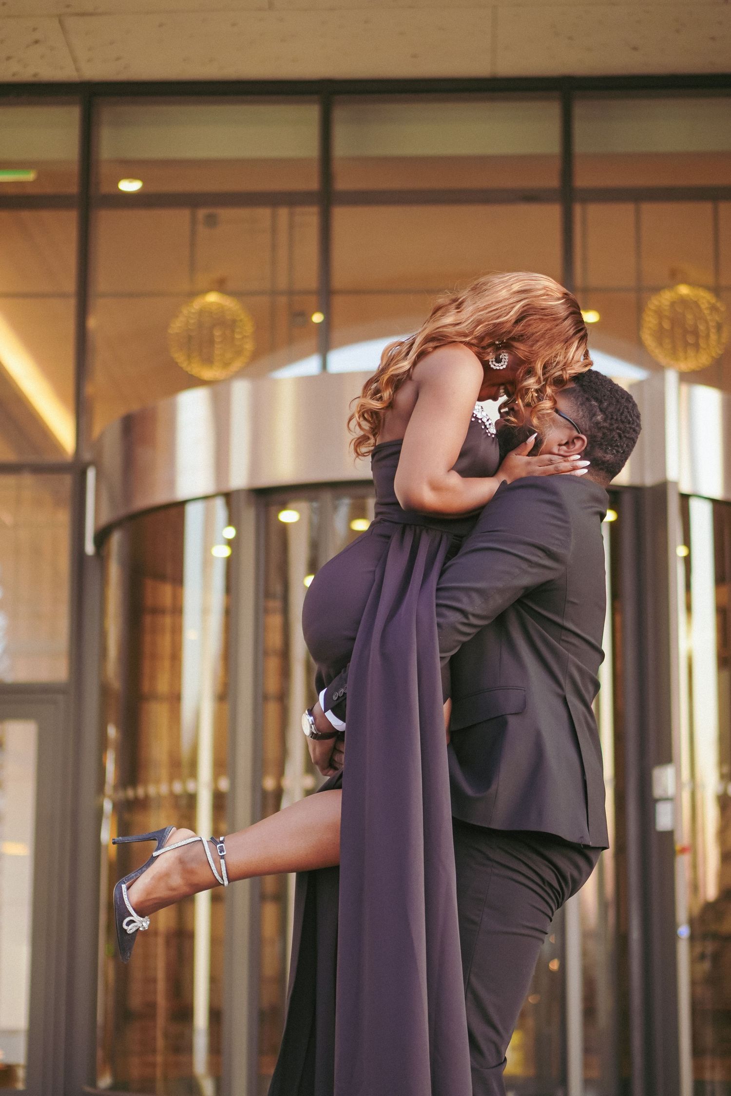 A romantic couple embracing in an elegant indoor setting with dramatic lighting and glass windows.