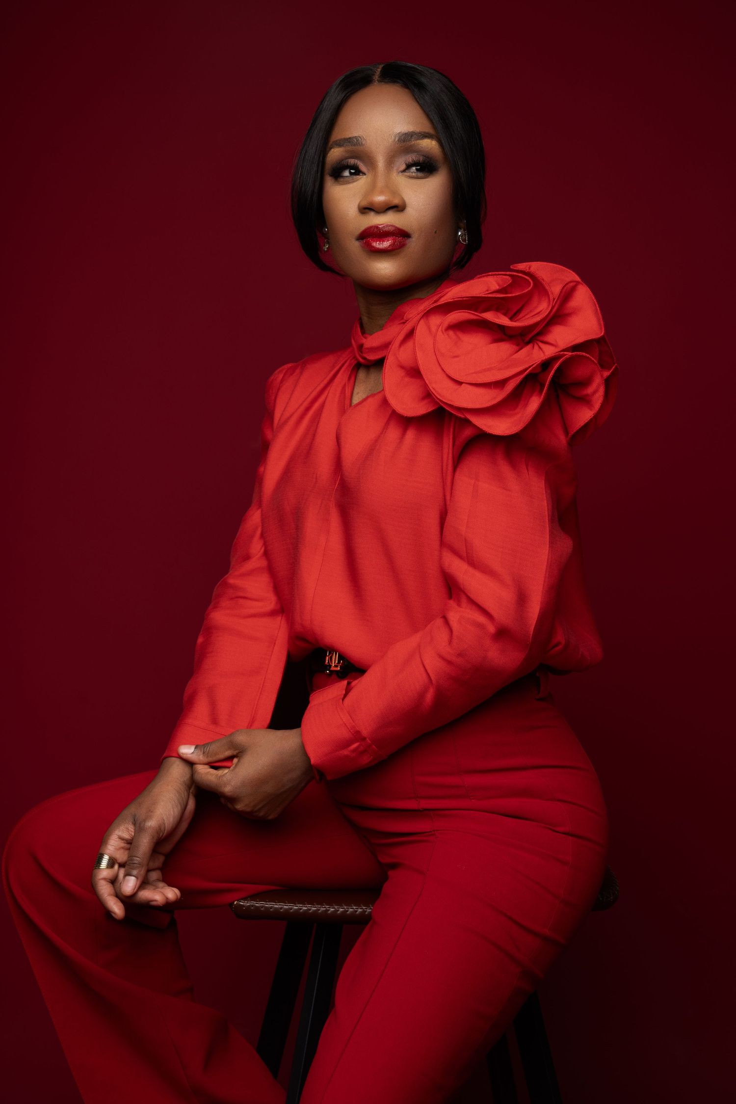 Dramatic fashion poses in a vibrant red outfit with statement shoulder detail against dark background.