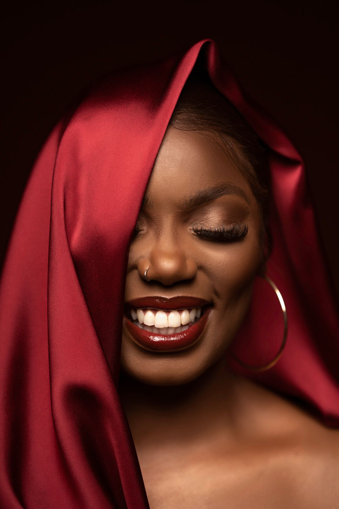 Dramatic close-up beauty portraits with red fabric and glowing skin.