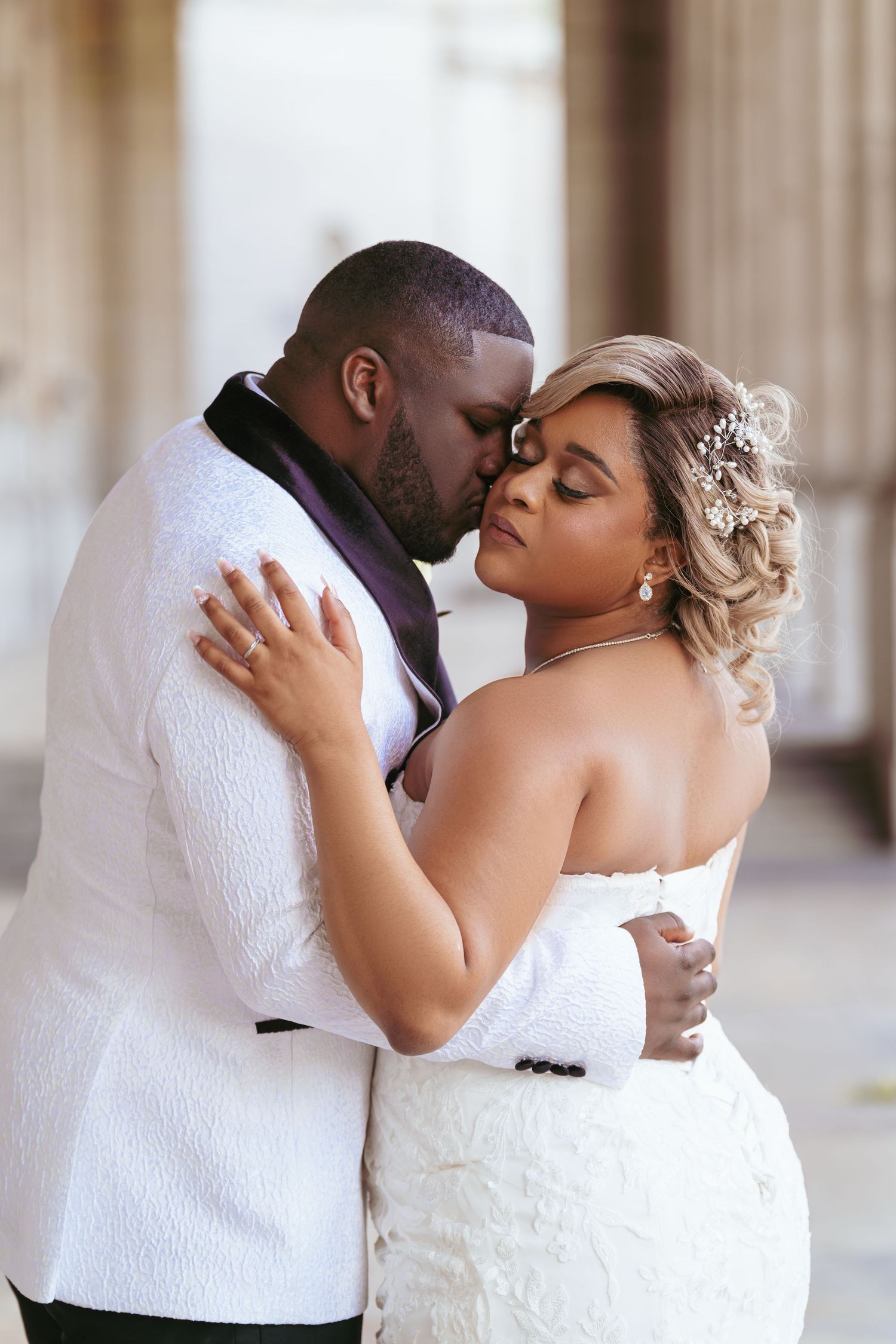 A couple in white wedding attire sharing romantic kisses during their wedding photoshoot.