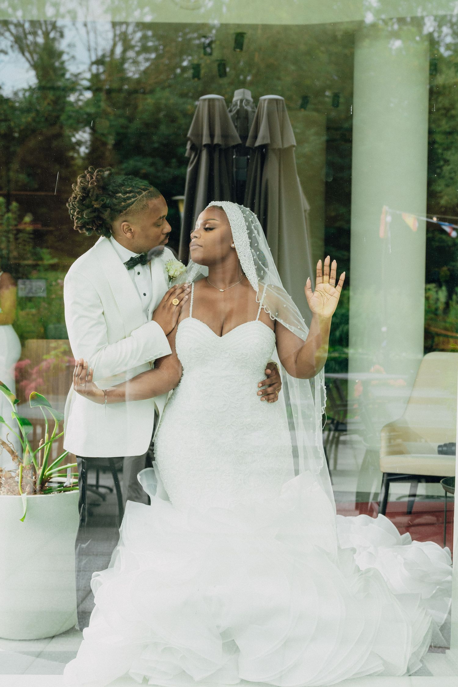 Joyful wedding moment captured through glass with couple in white attire.