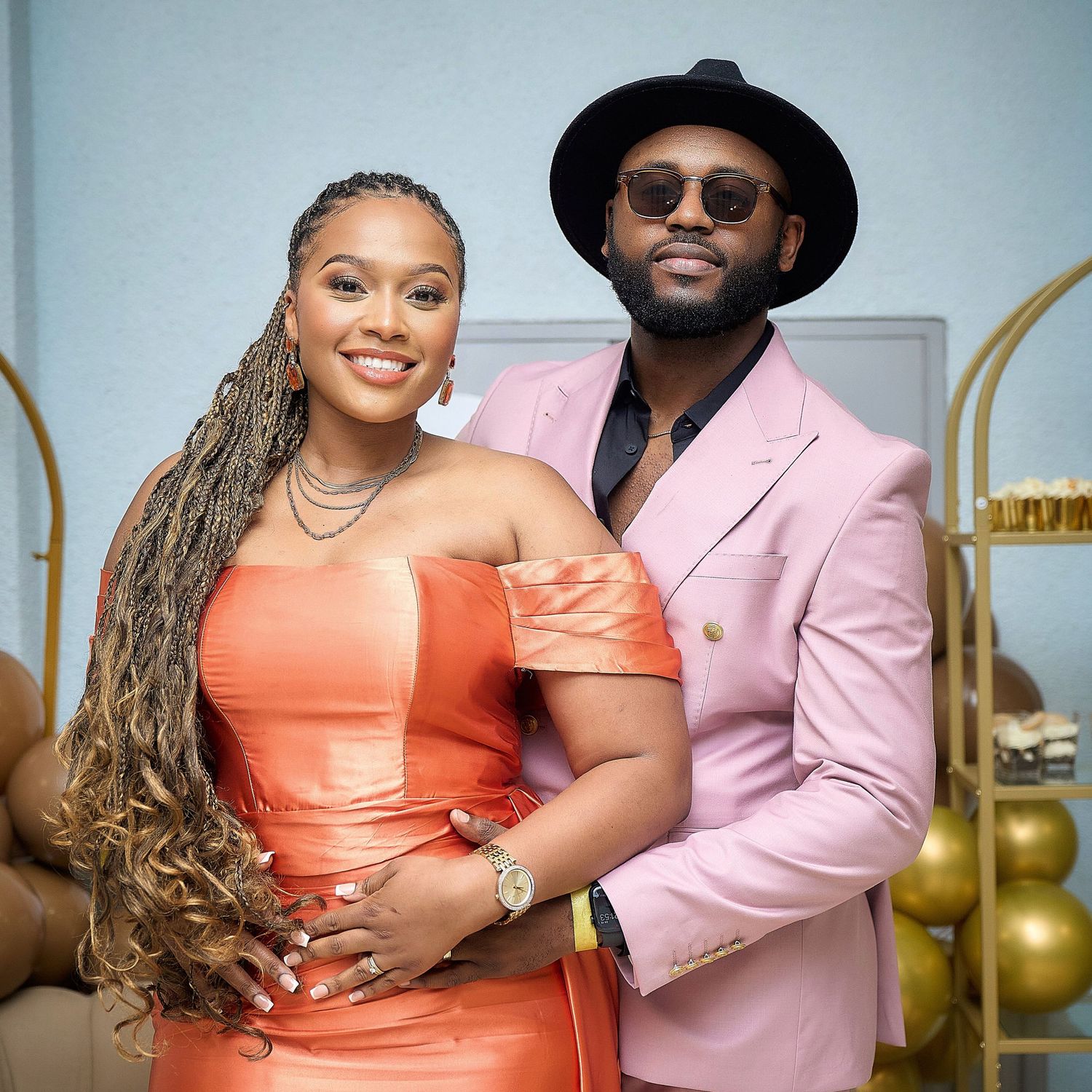 Romantic couple poses in coordinating coral and pink formal attire against a light backdrop.