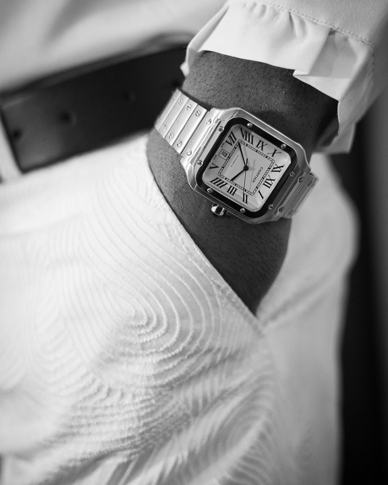 Close-up of square silver watch against white textured fabric in black and white.