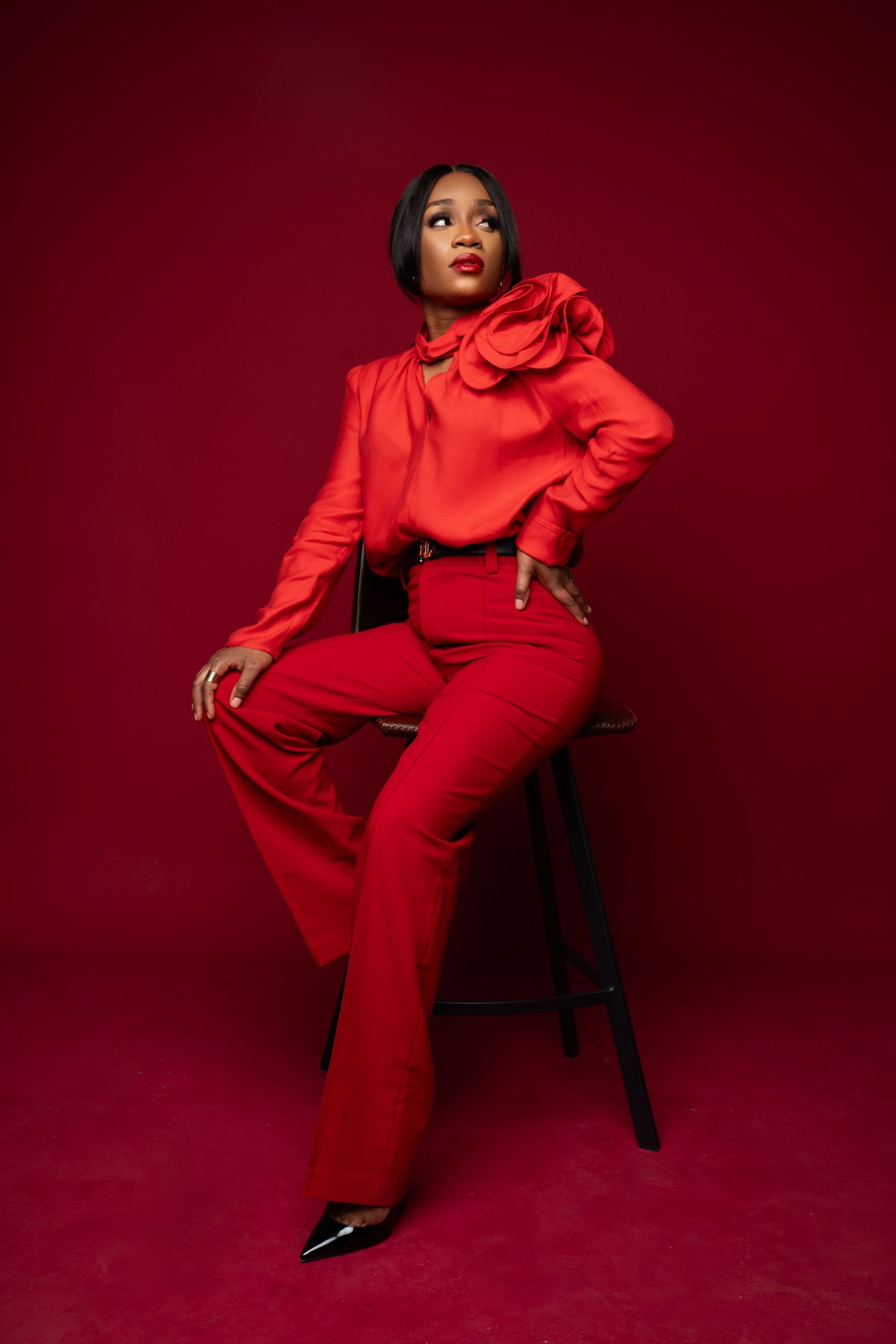 Fashion photoshoot featuring a striking red pantsuit against a deep burgundy backdrop.