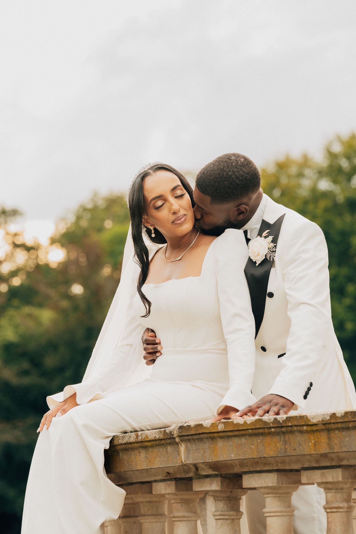 A couple in wedding attire sharing intimate moments on a stone balcony during an outdoor photoshoot.