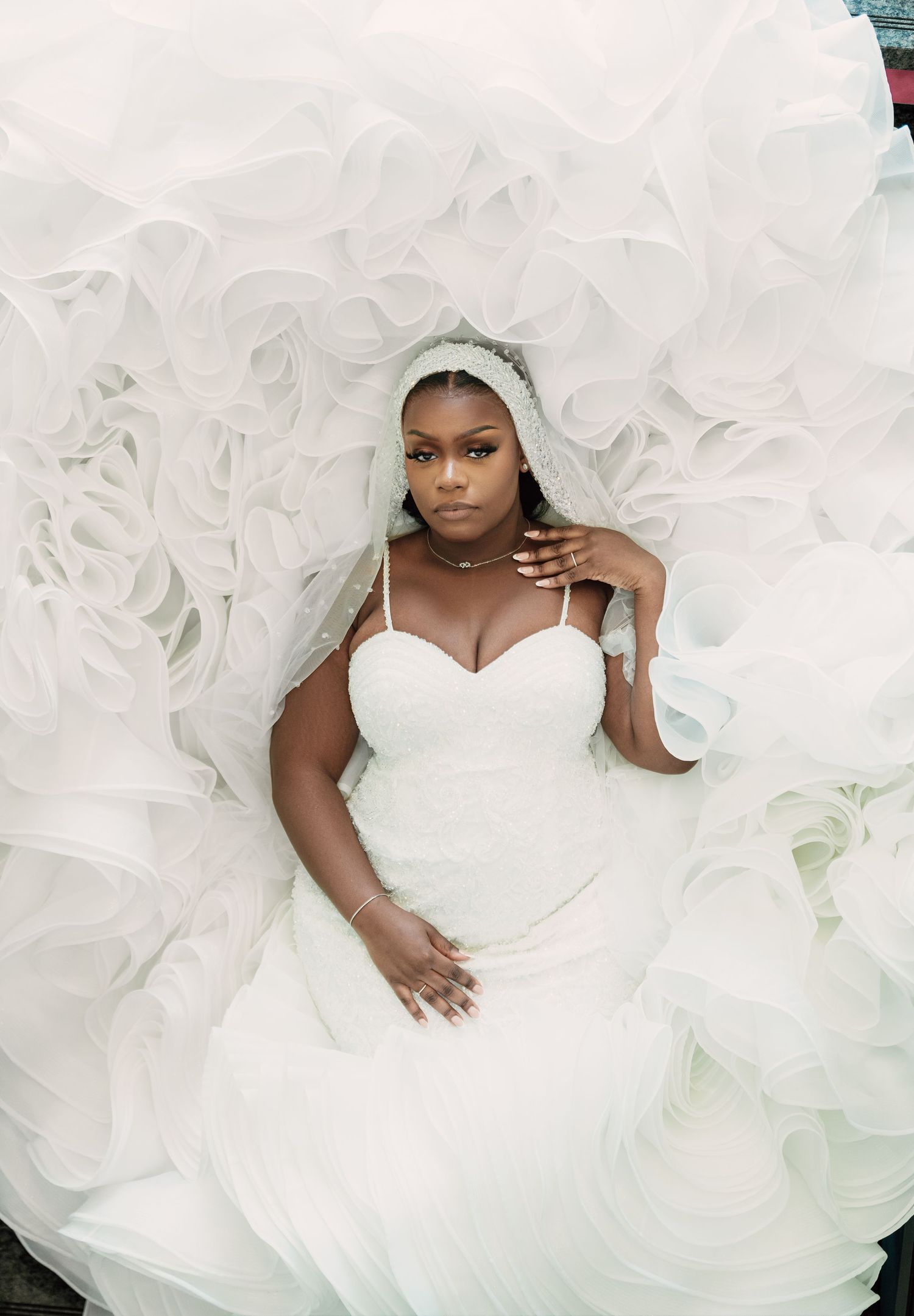 A bride in a voluminous white wedding gown with ruffled tulle details poses for bridal portraits.
