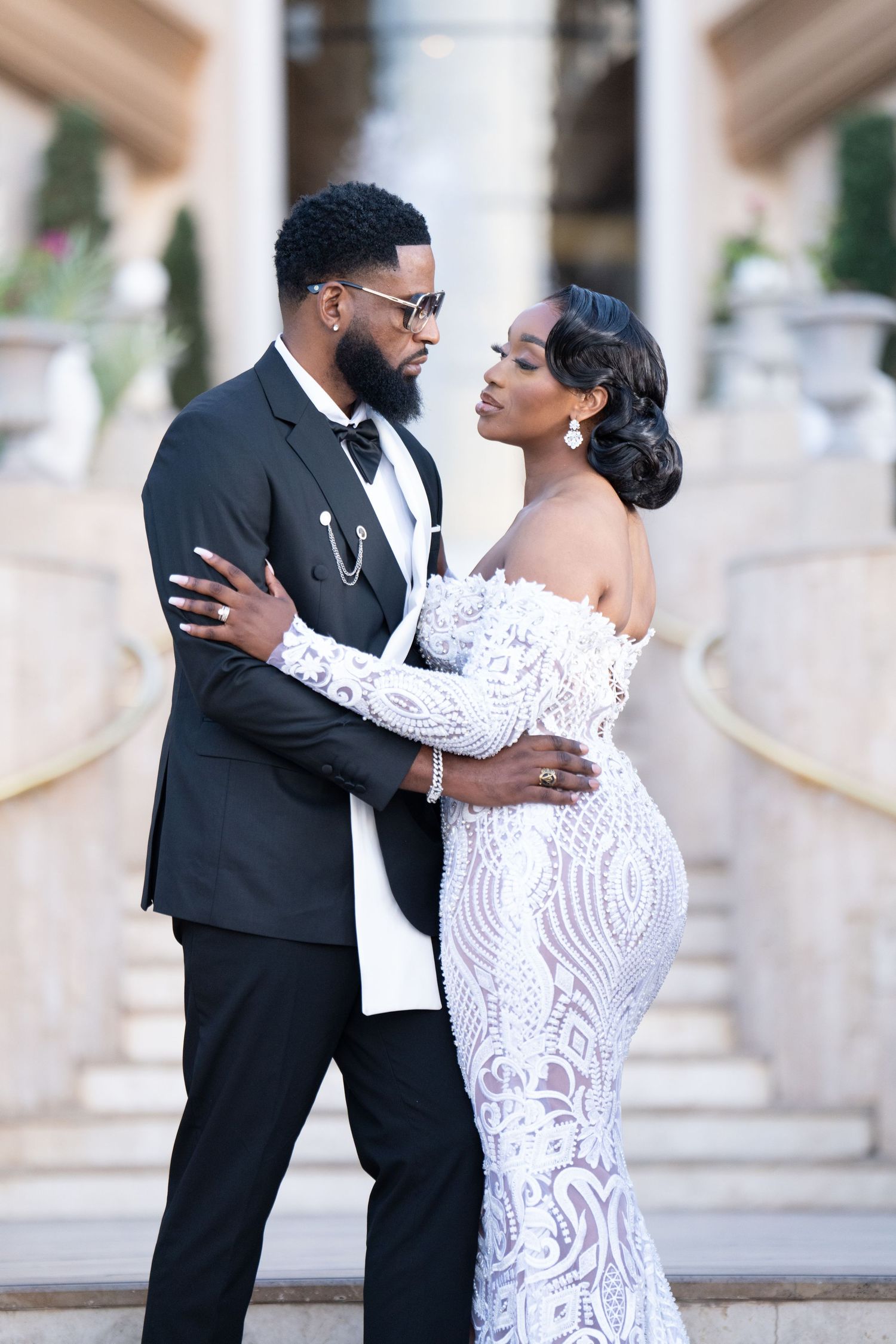 Romantic wedding couple embracing in formal attire against white pillars.