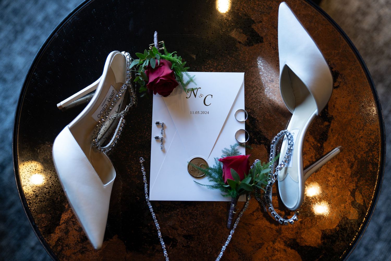 White bridal heels and wedding accessories arranged on a dark rustic surface.