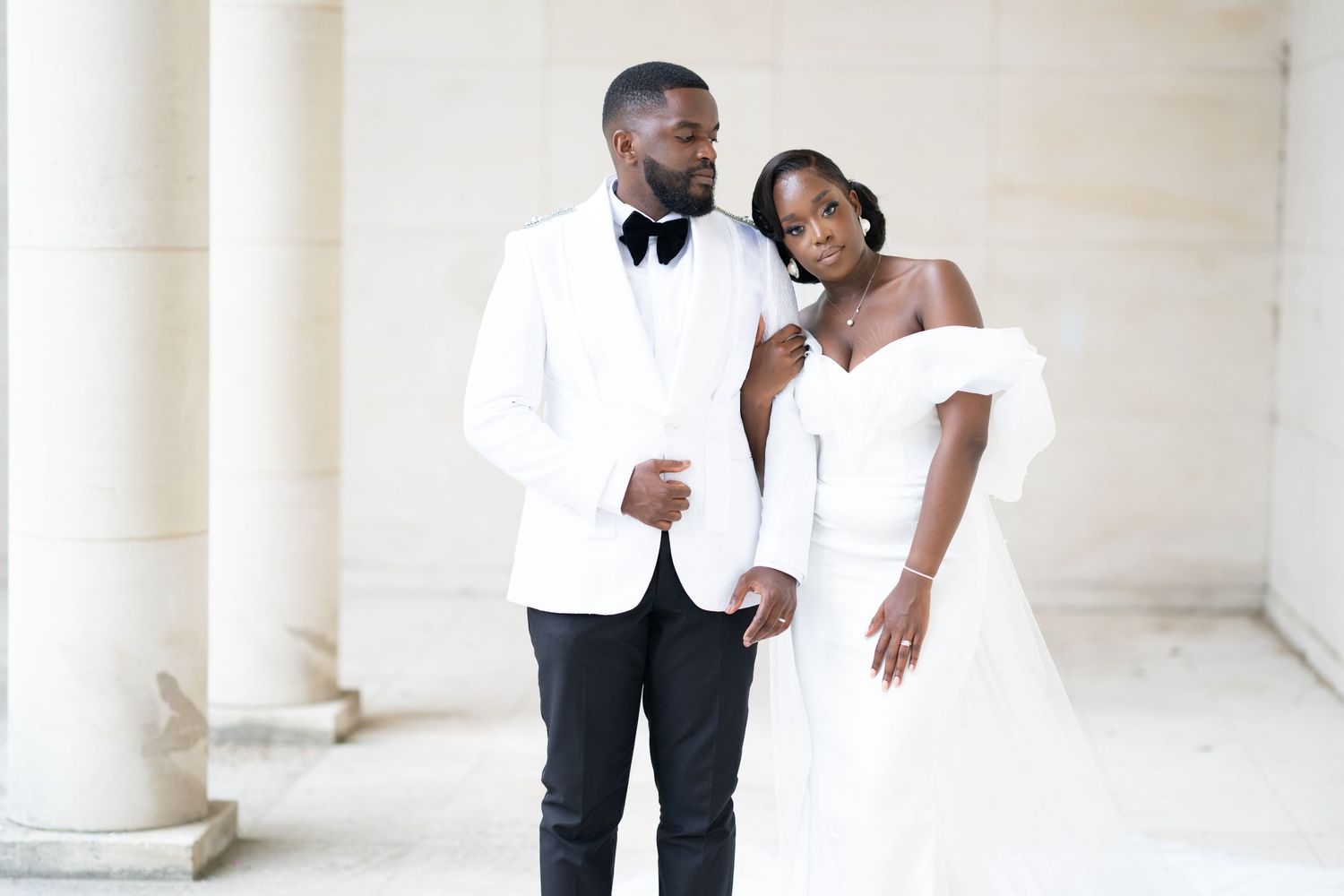 Elegant couple poses in formal wedding attire against classical white columns.