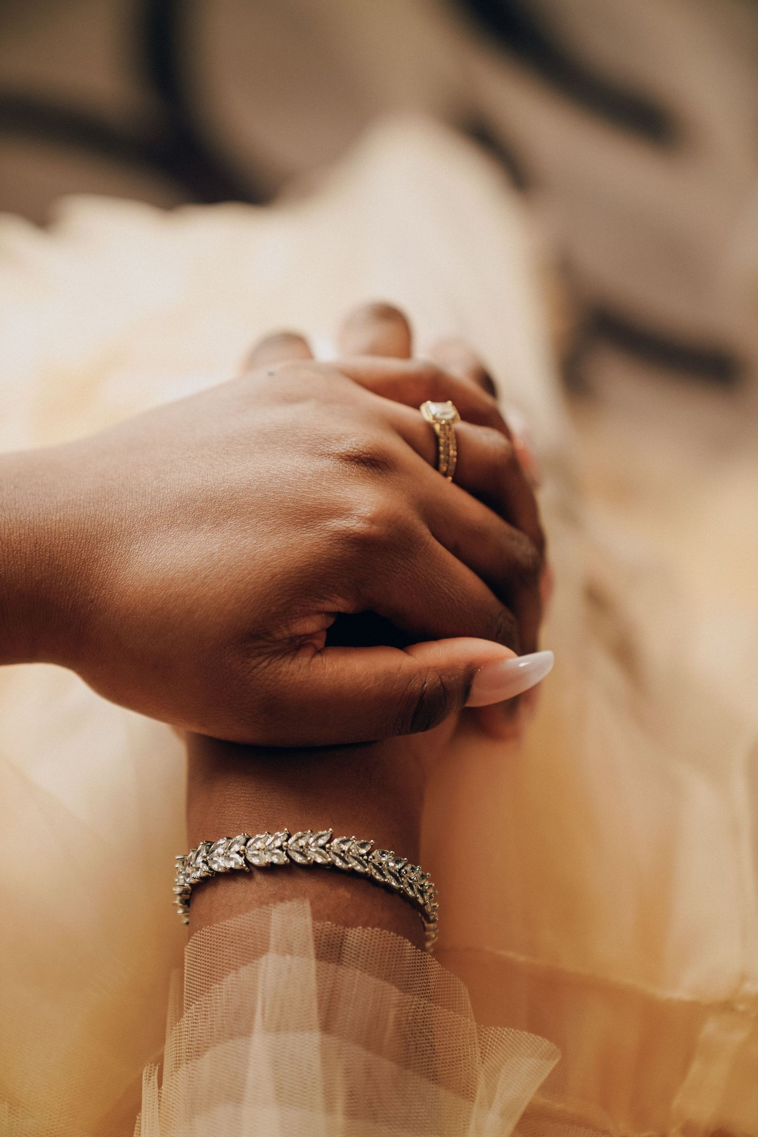 Close-up of hands wearing elegant jewelry and rings against a soft beige background.