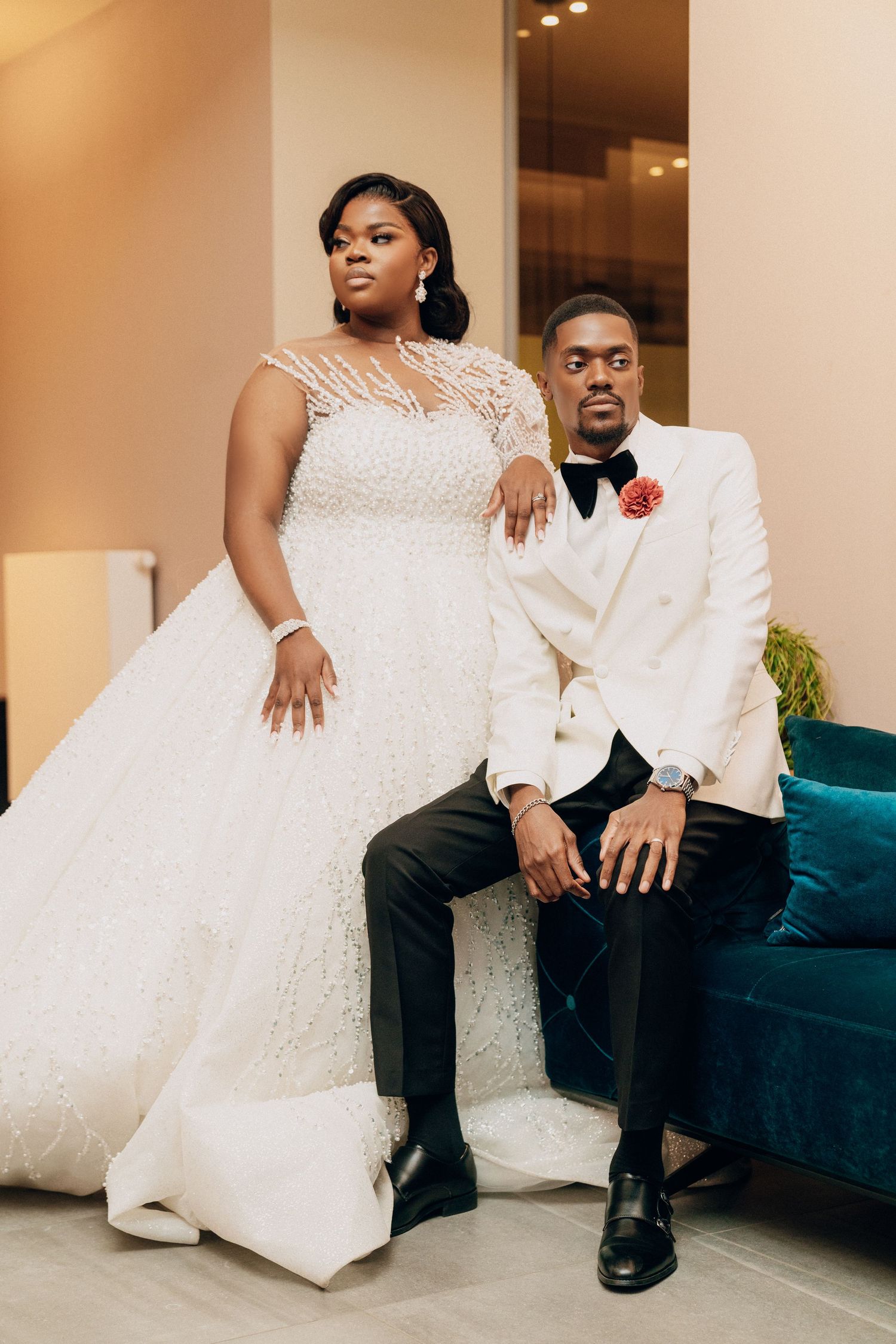 Wedding couple poses intimately on blue velvet couch in formal attire.