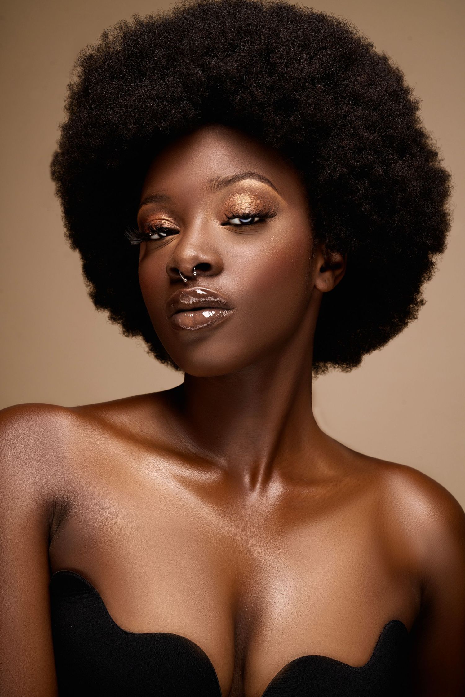 Beauty portrait of model with natural afro hairstyle and glowing makeup against brown background.