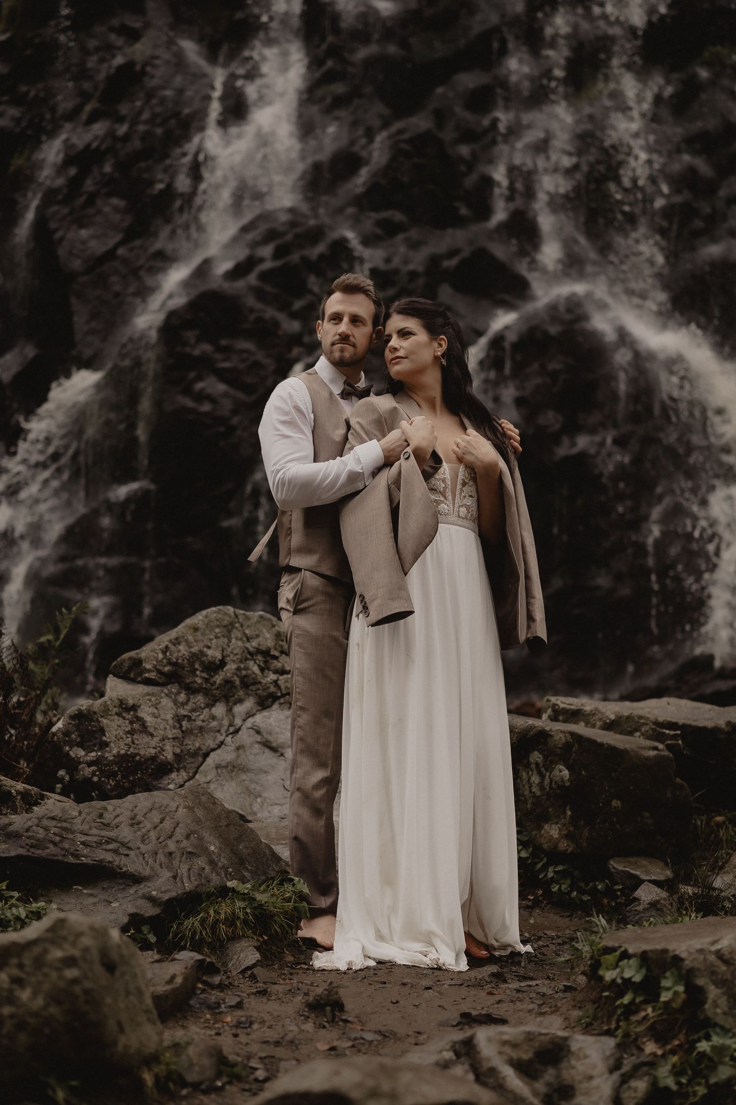 A romantic couple embraces on a rocky cliff with dramatic dark cliffs in the background.