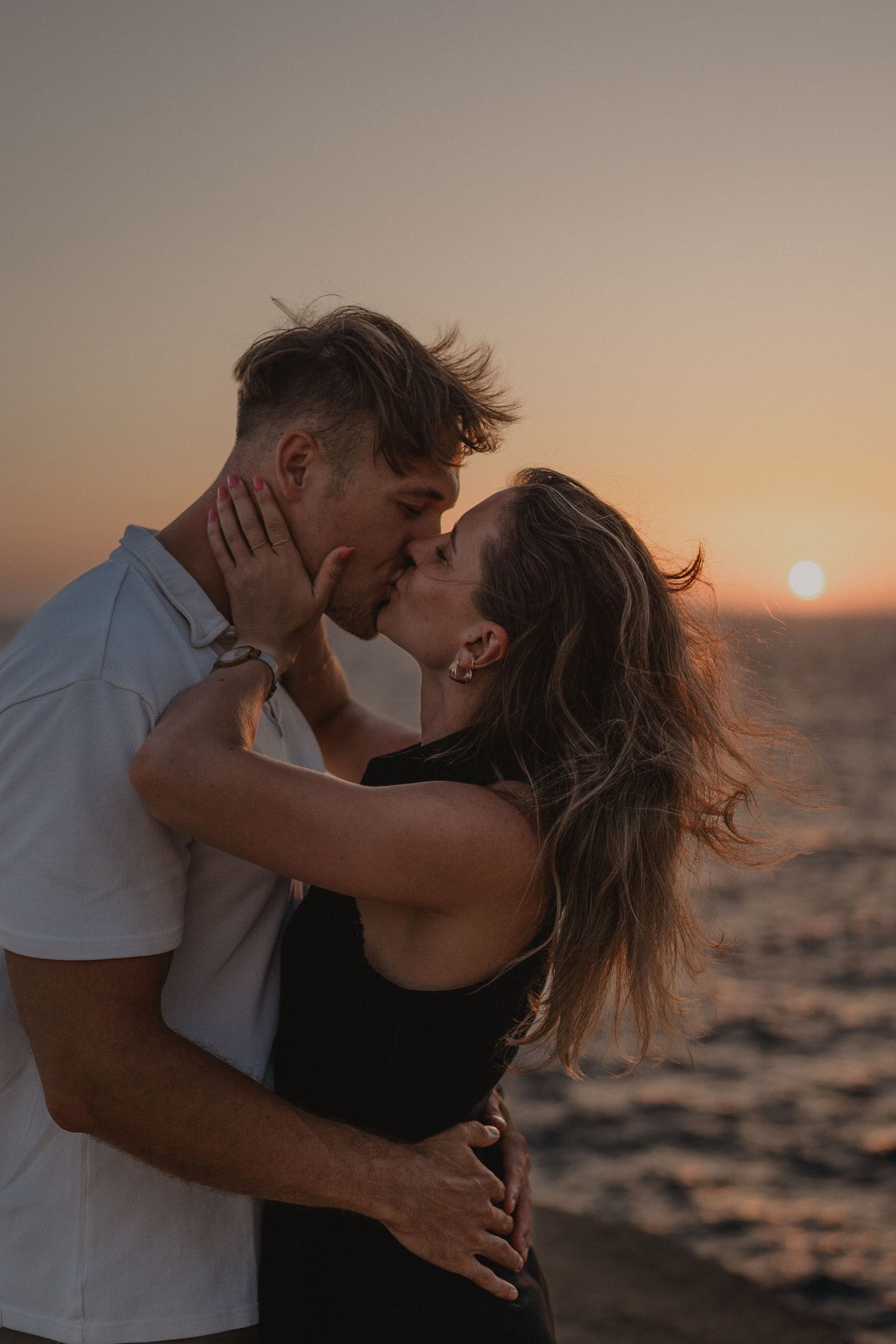 Couple sharing a romantic kiss at sunset by the ocean, with warm golden hues and gentle sea breeze.