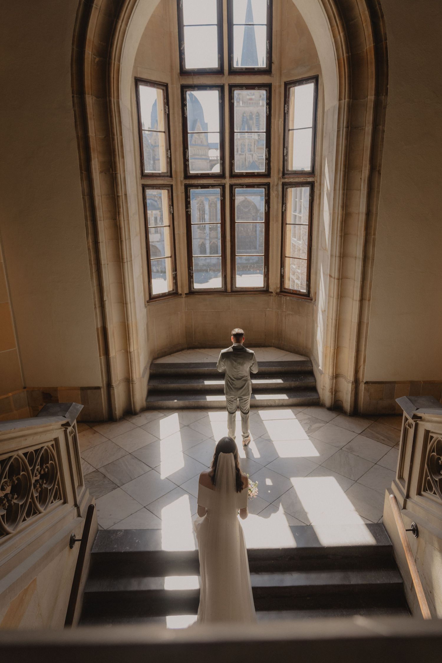 Architectural wedding photo in grand arched window staircase with dramatic lighting.
