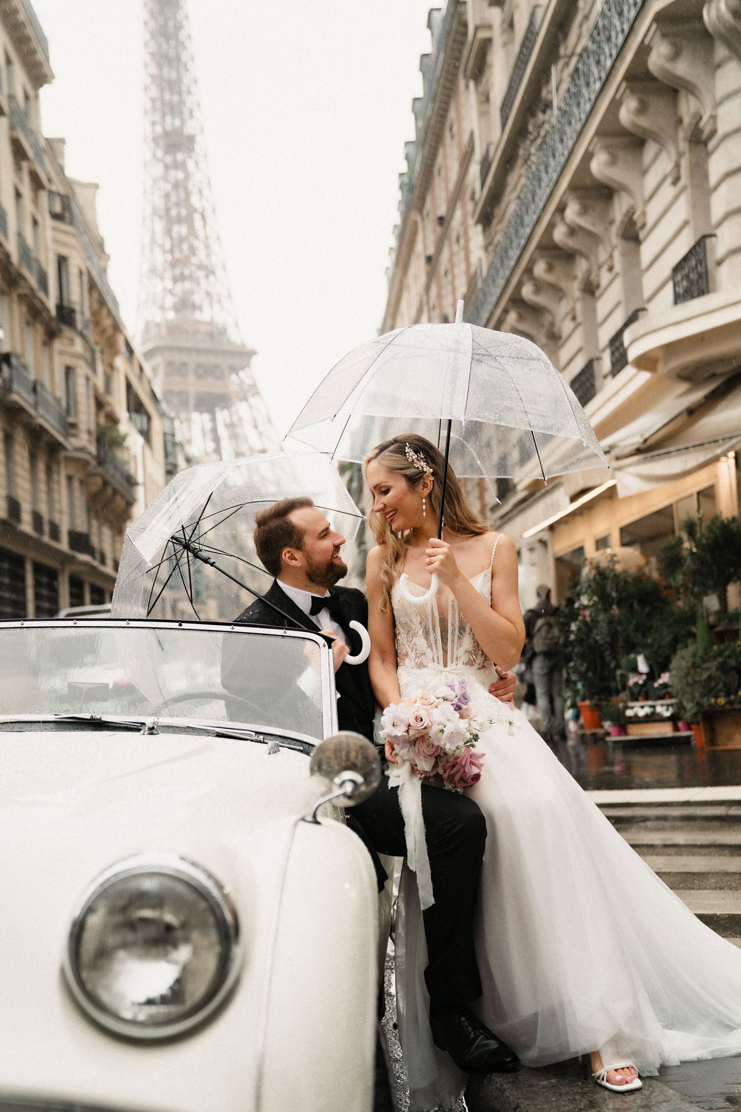 A romantic wedding photoshoot in Paris with a vintage car and the Eiffel Tower visible in the background.