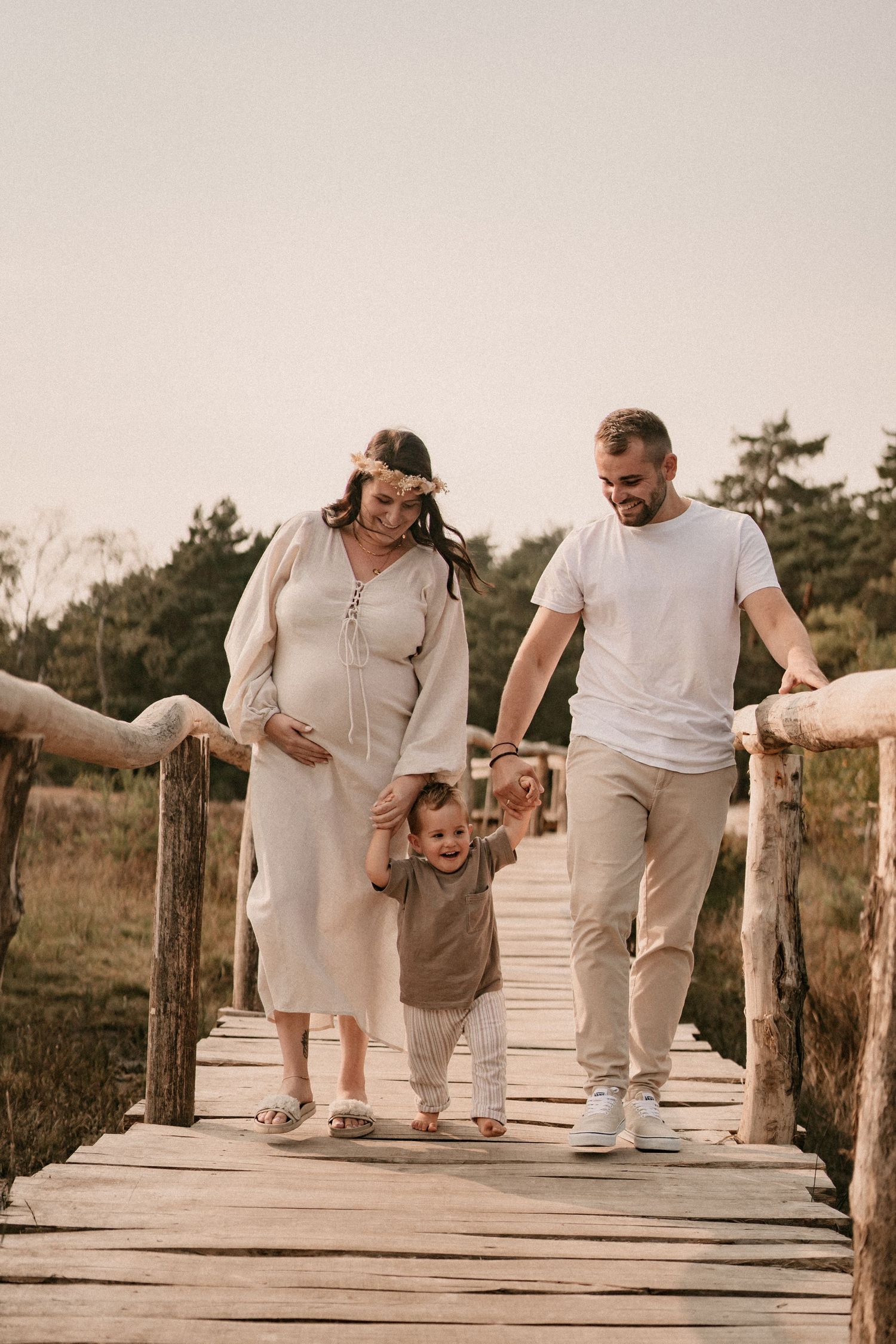 Family walking and playing together on a wooden boardwalk during a sunset photoshoot.