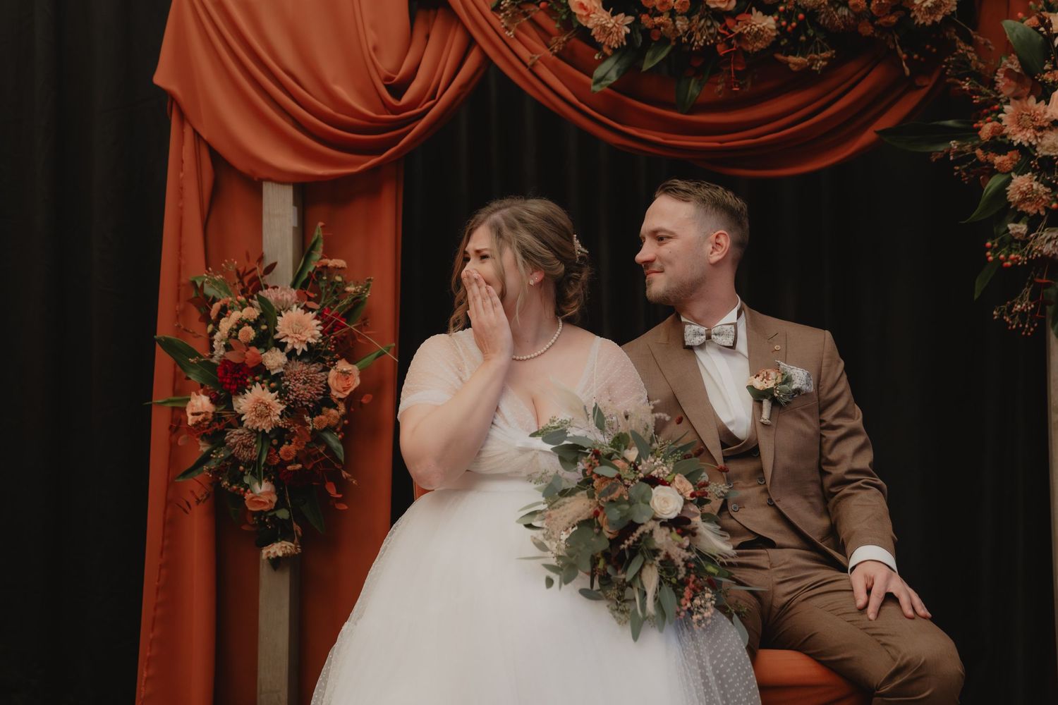 Wedding celebration with terracotta draping and lush floral arrangements in moody lighting.