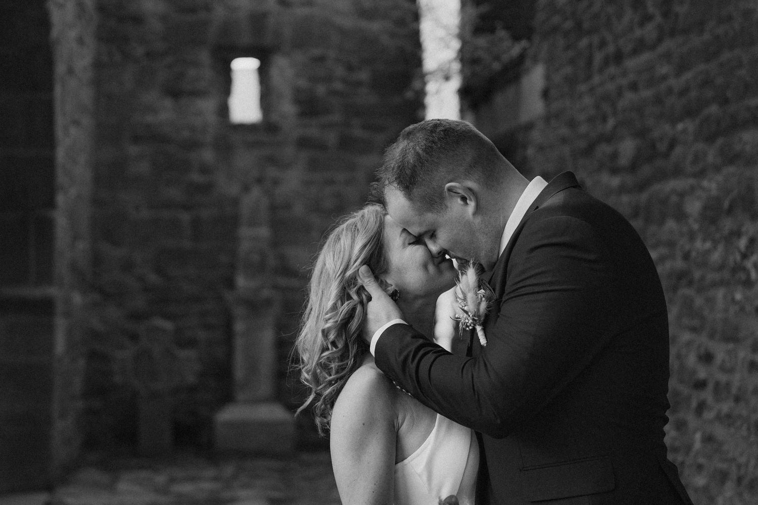 Intimate black and white wedding portrait captured against textured brick wall background.