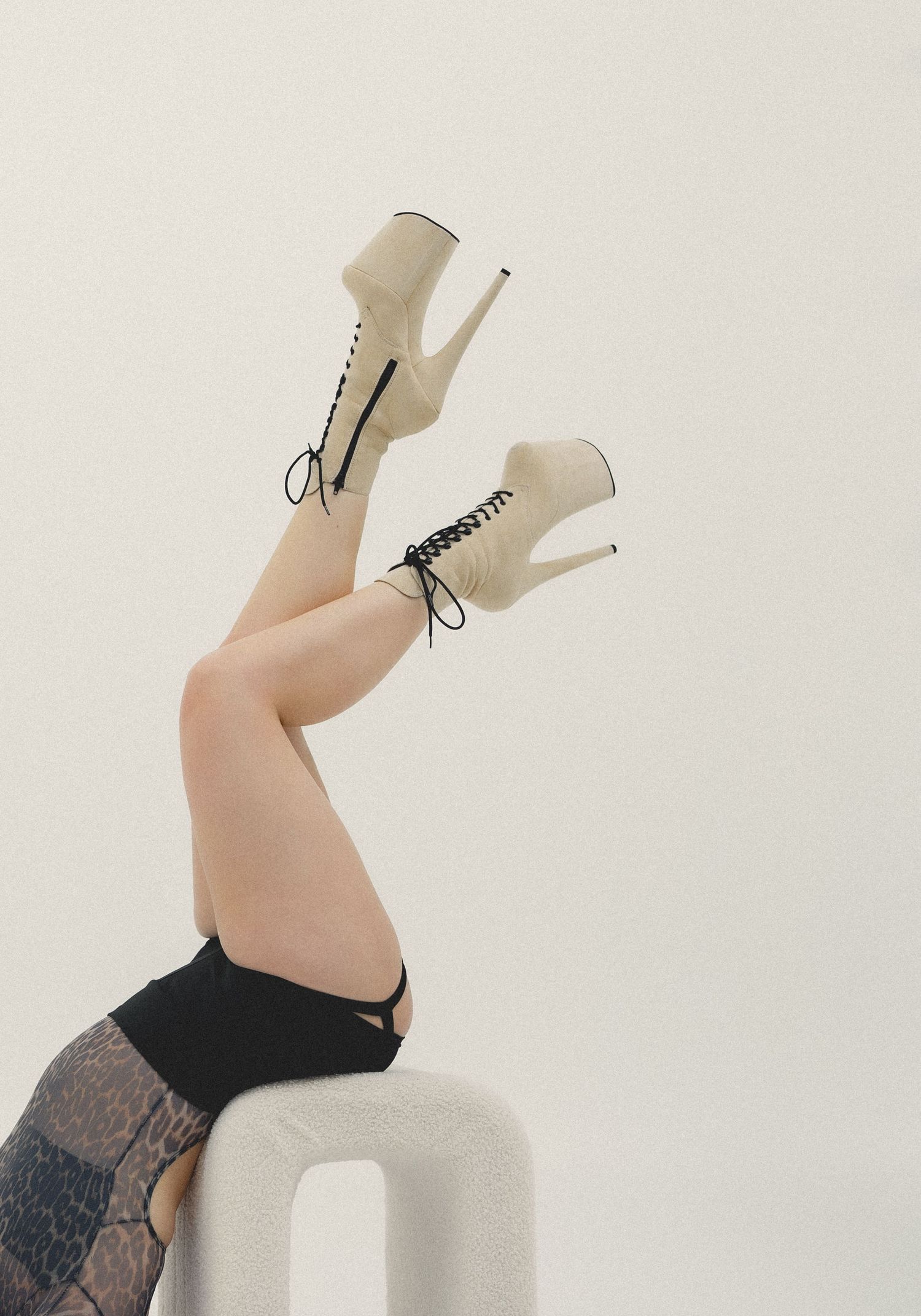 Legs raised up wearing cream lace-up stiletto ankle boots with lace tights on a white stool.