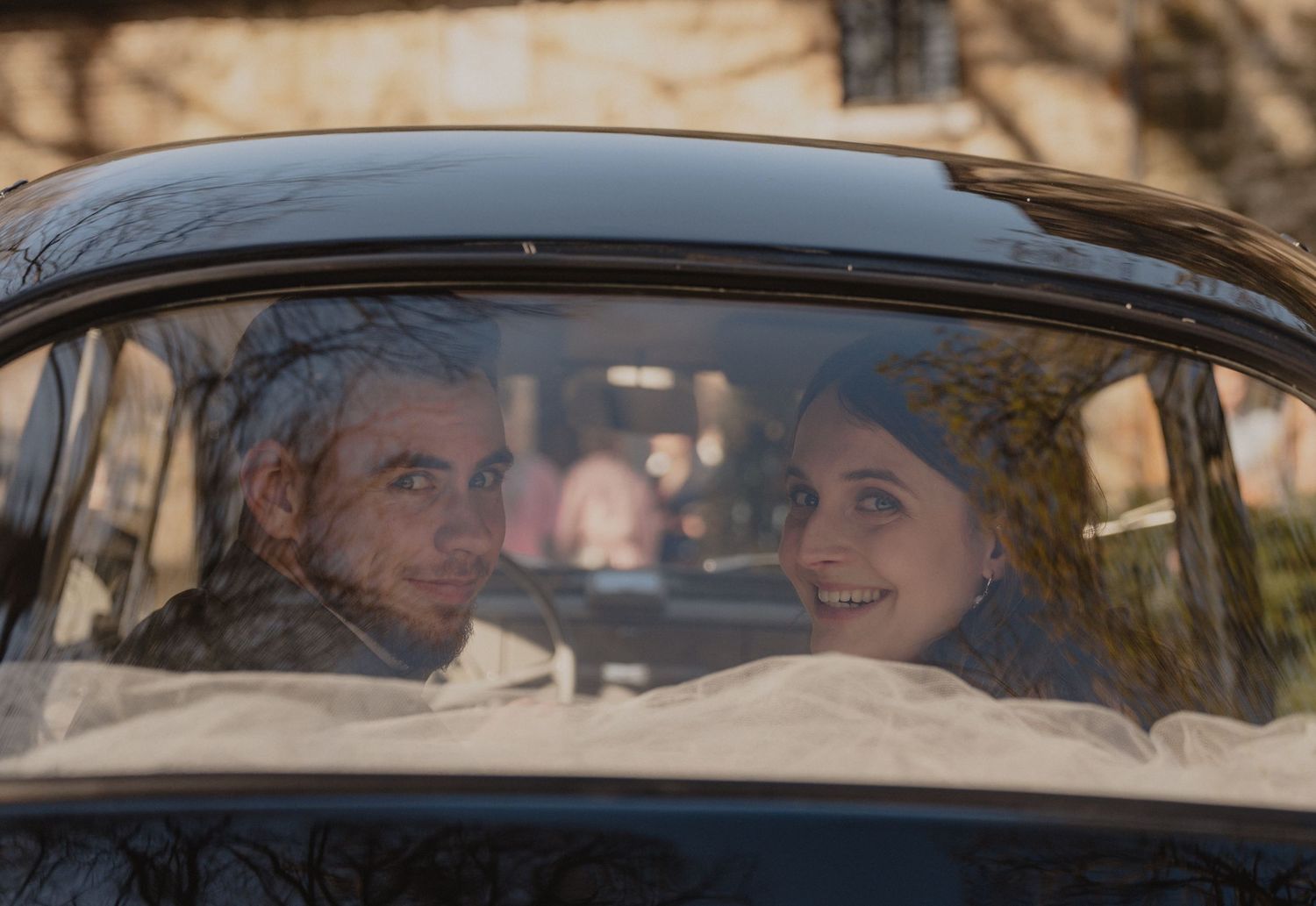 Wedding couple seen through a vintage car window with floral decorations.