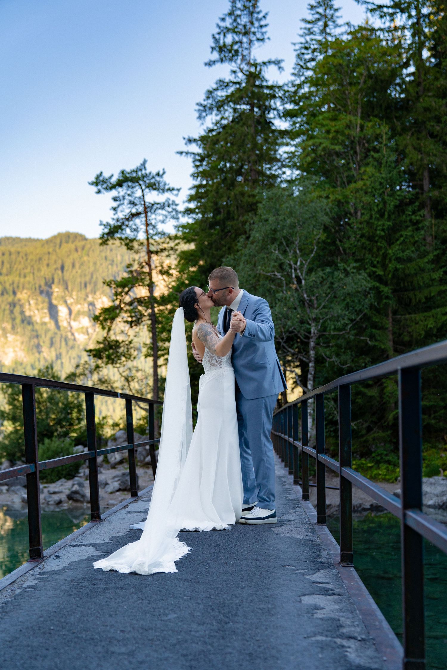 Newlyweds share tender moments on a mountain viewpoint surrounded by evergreen forest.