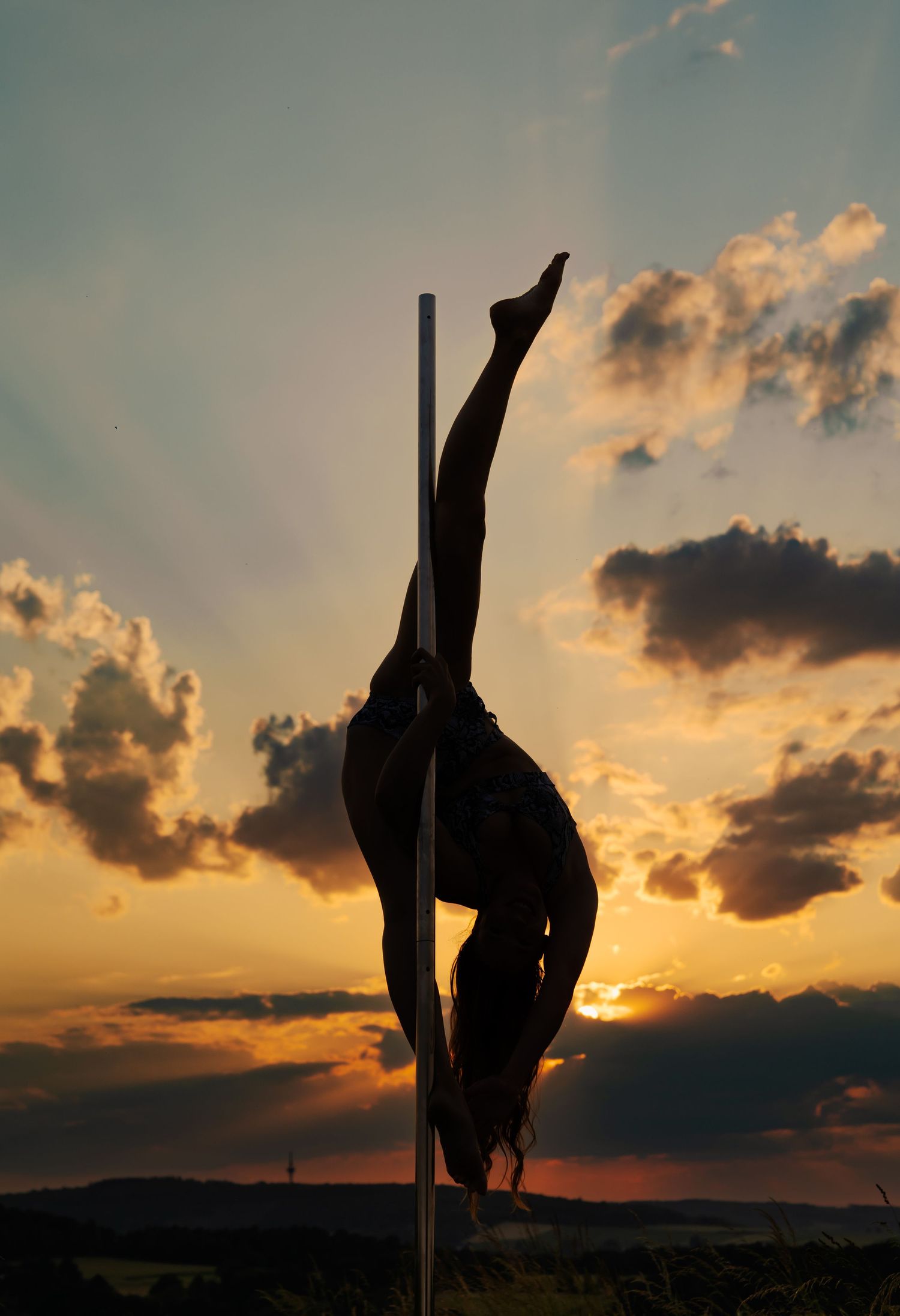 Silhouette of a pole dancer performing an elegant split against a dramatic sunset sky with golden clouds.