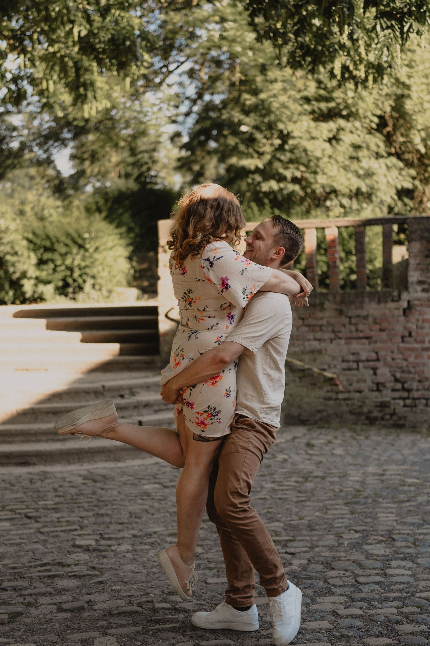 Playful couple dancing and spinning on cobblestone ground during golden hour.