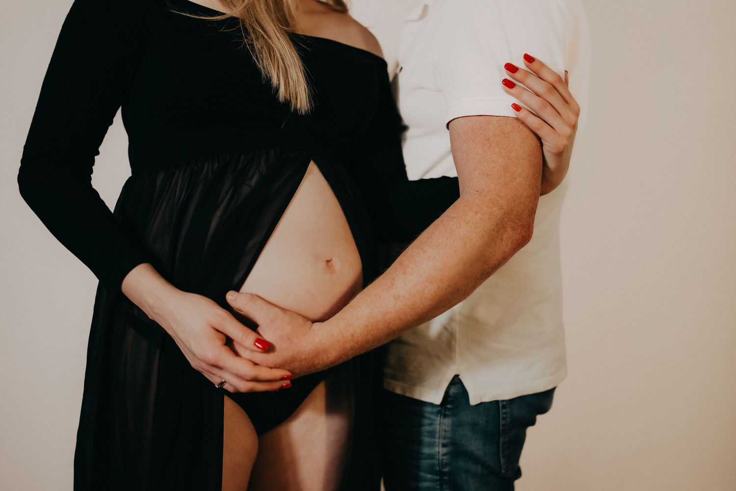 Intimate maternity photo shoot with couple embracing against neutral background.