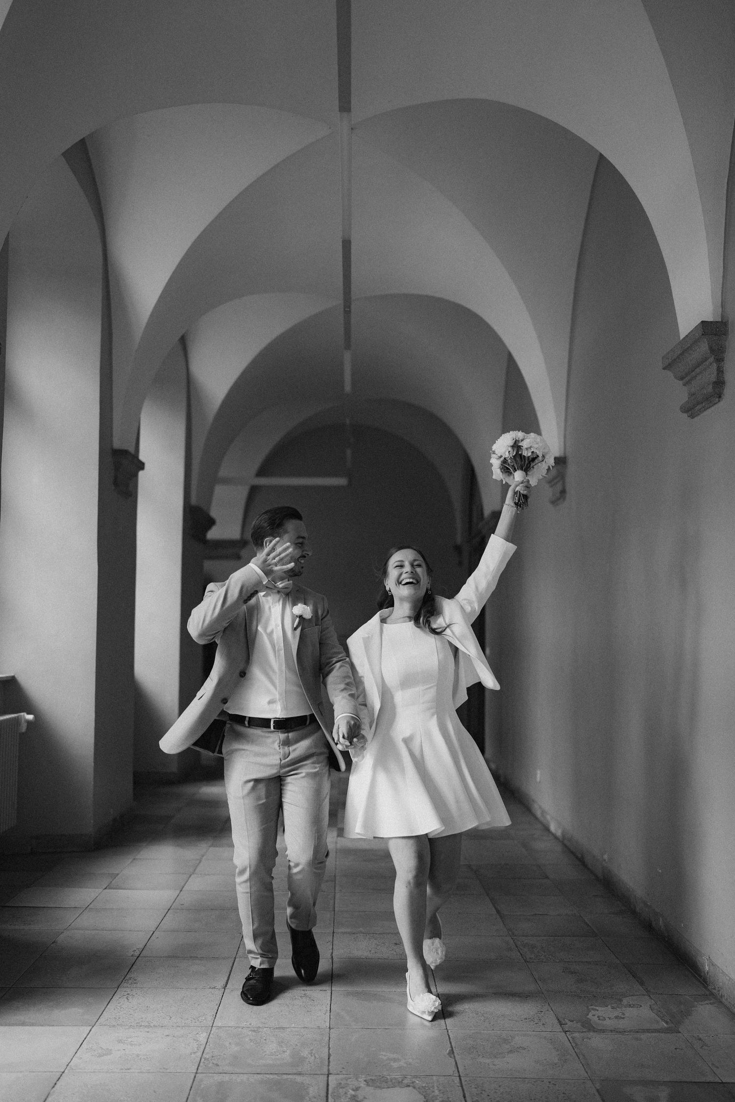Couple dancing playfully in a hallway with arched ceilings and natural lighting.