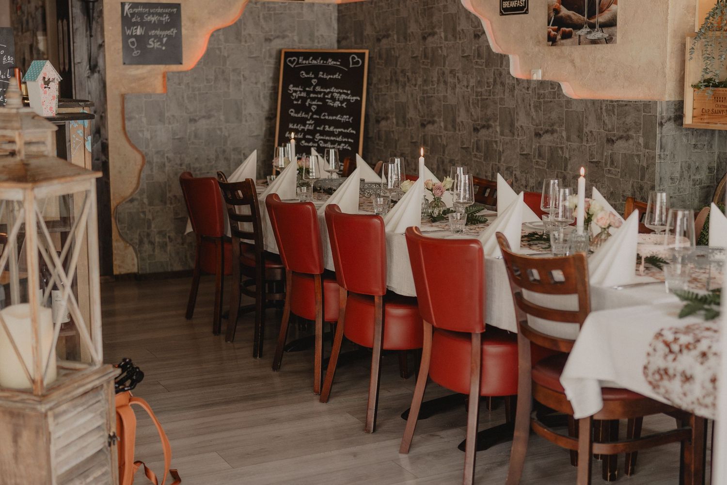 Wedding reception venue with elegant table settings and red chairs against rustic stone walls.