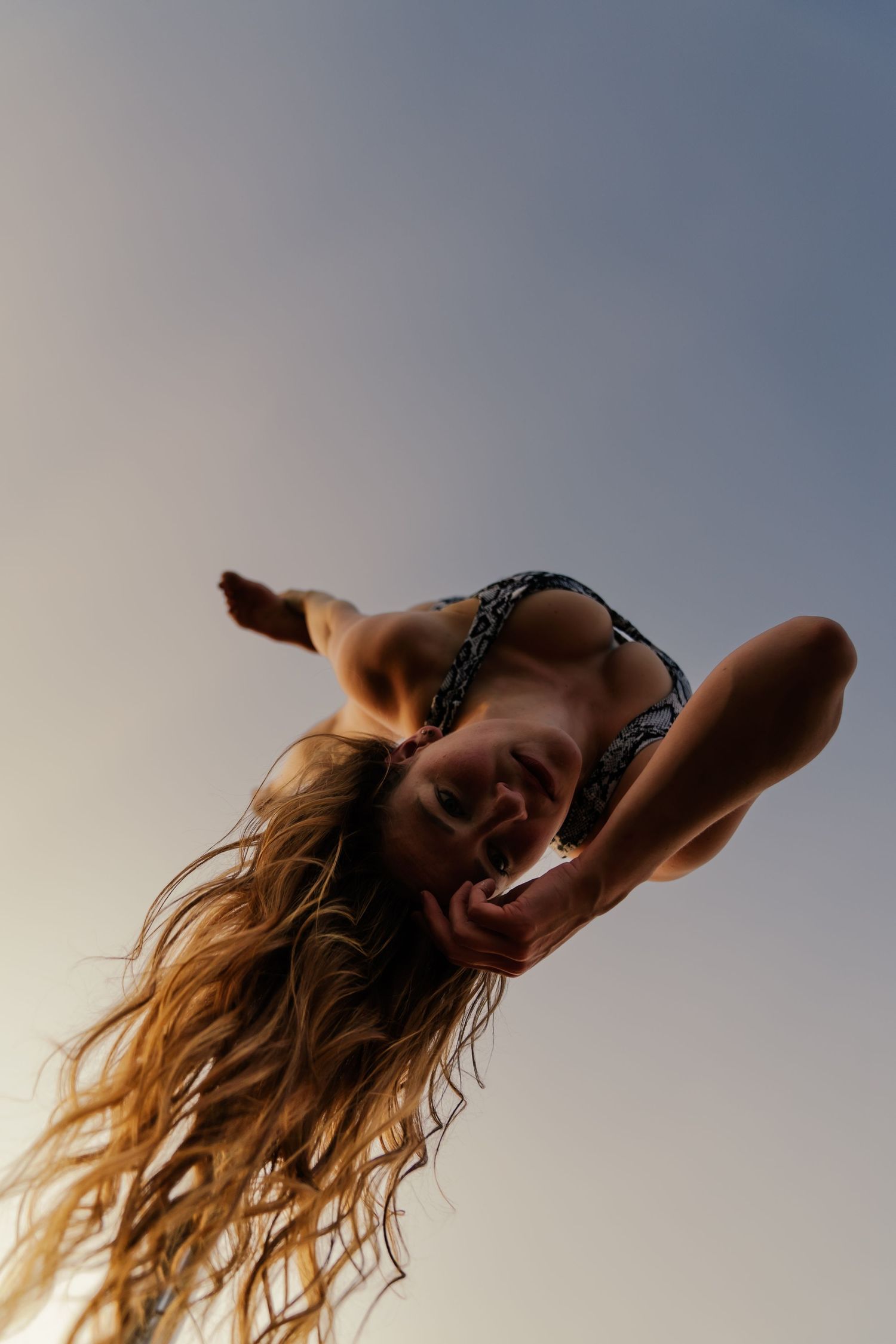 Young woman in bikini top with flowing hair photographed from below against a clear sky backdrop.